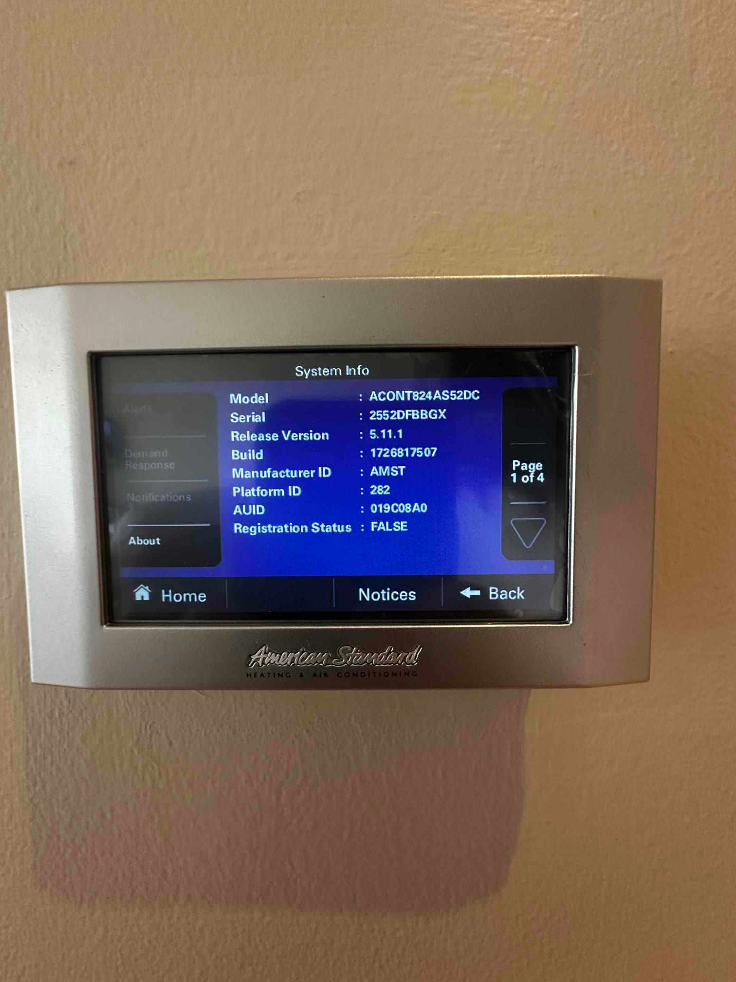 Wall-mounted touchscreen thermostat displays system information menu after installation, showing model, serial, and software version details.