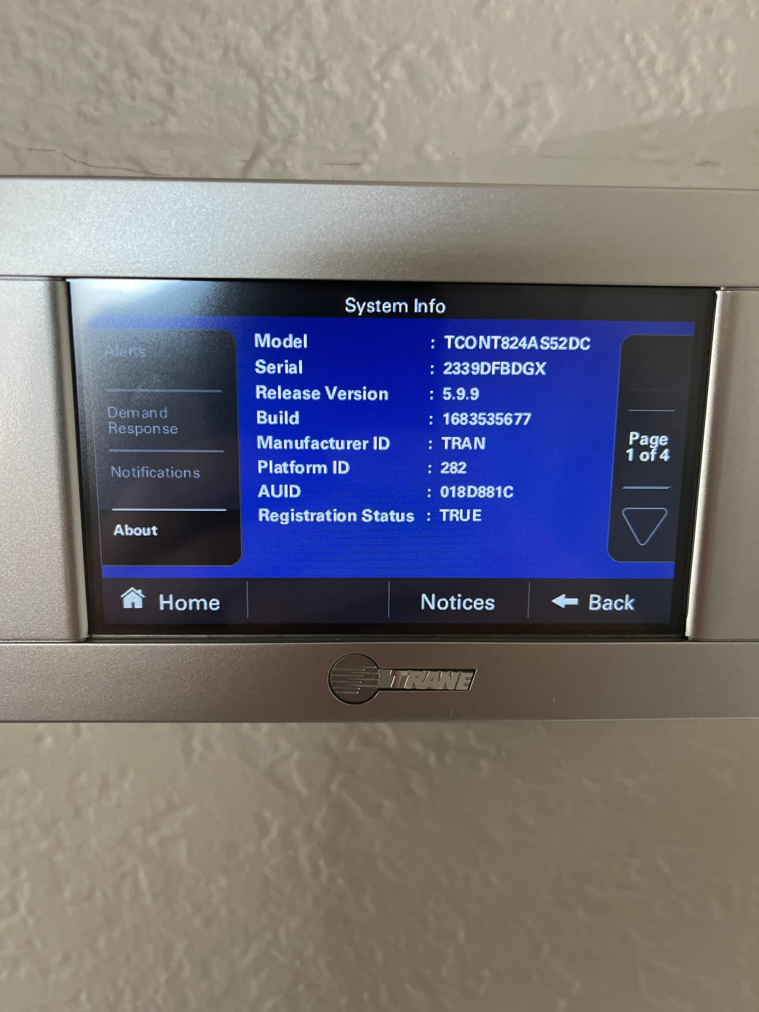Wall-mounted touchscreen thermostat displays system information on the screen after setup, confirming successful installation and registration.