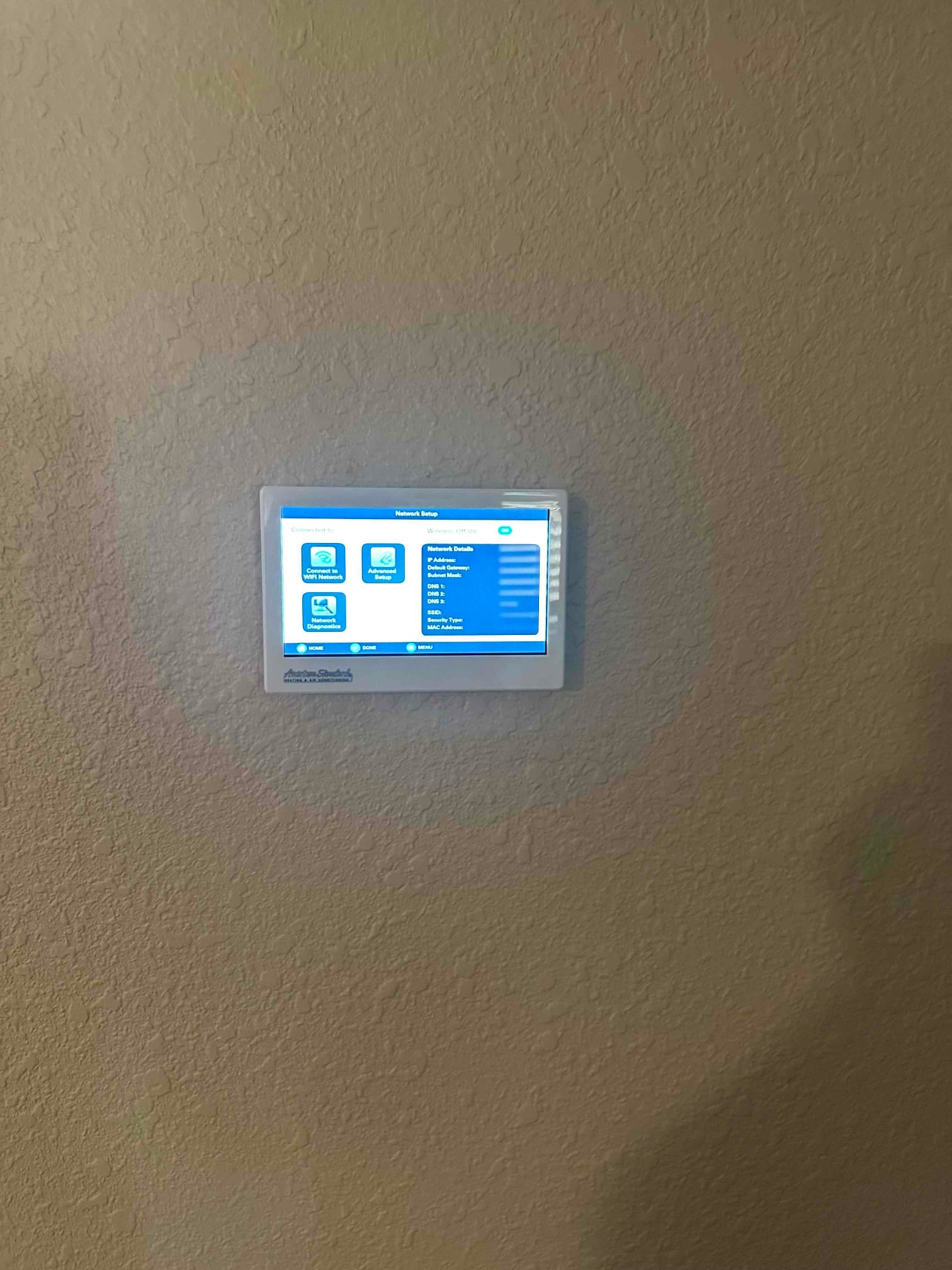 Wall-mounted touchscreen thermostat powered on, showing on-screen setup menus following installation.