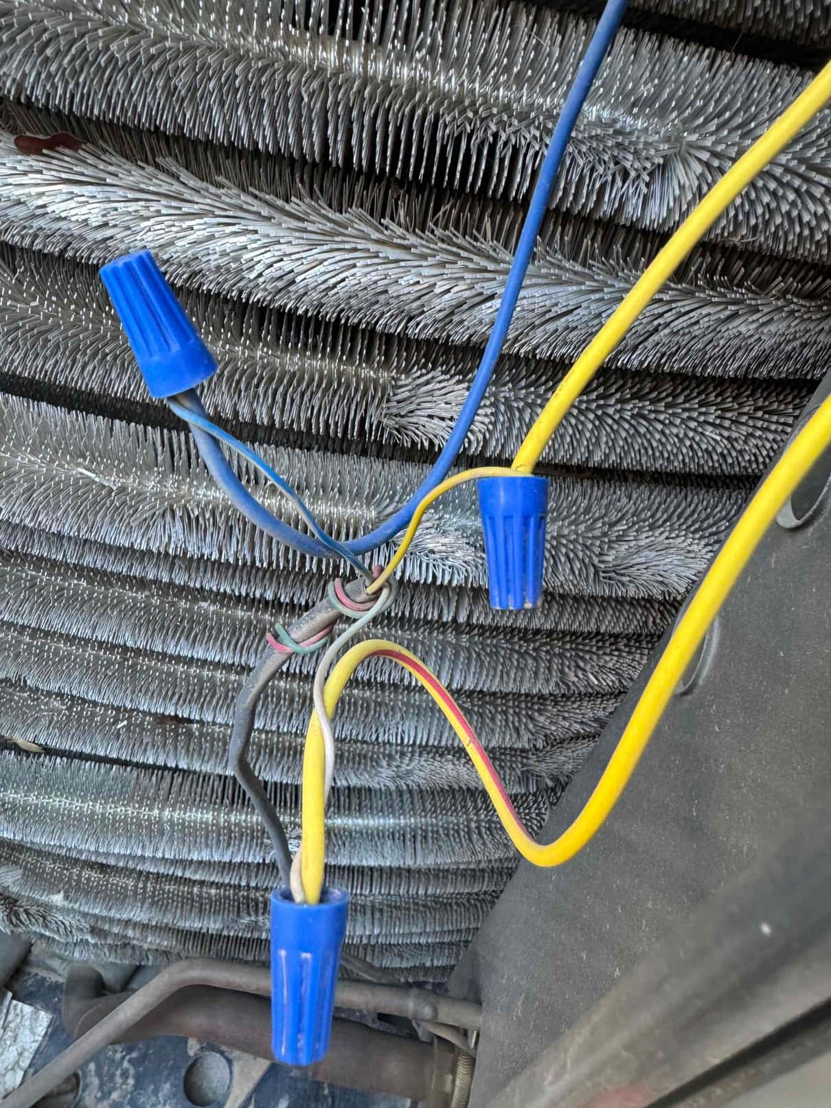 Wire connections with blue wire nuts in front of an outdoor condenser coil with bent fins visible.