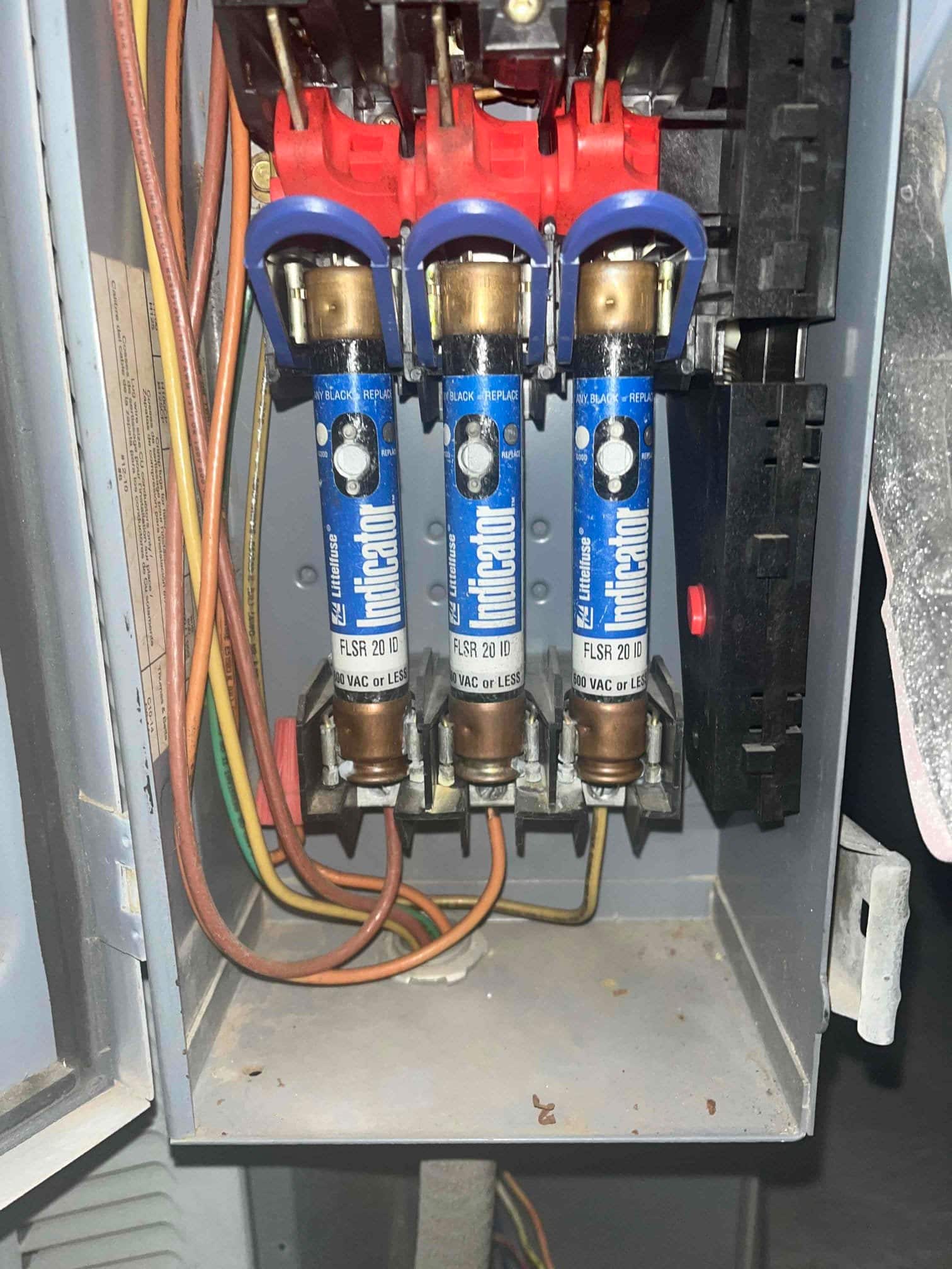 Three cartridge fuses installed in a fused disconnect enclosure with connected conductors visible at the terminals.