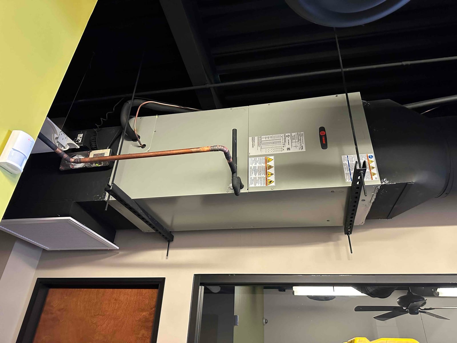 Ceiling-hung air handler installed with insulated duct connections, copper line set, and support brackets secured to the structure.