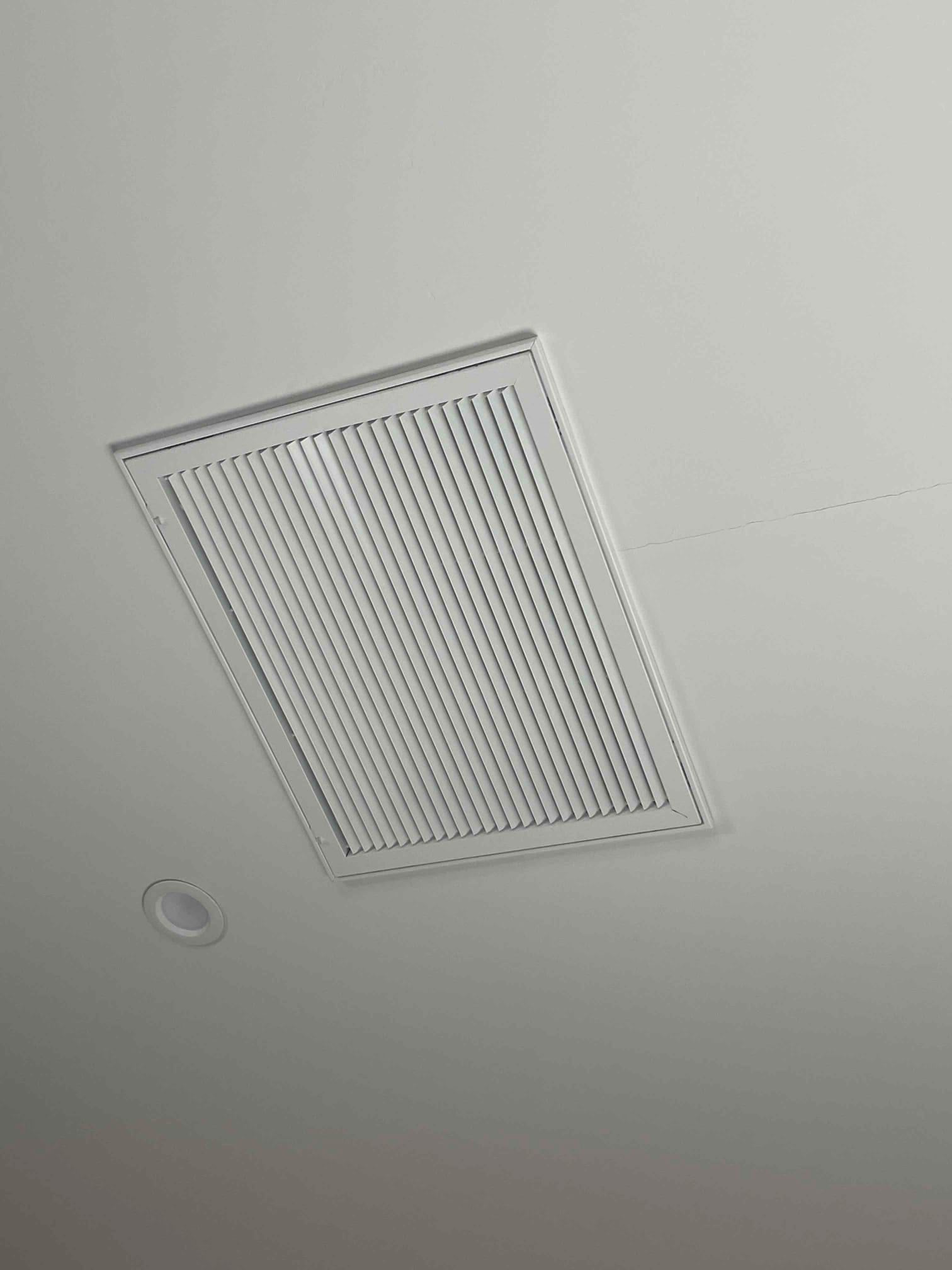 Ceiling return grille installed flush with drywall near a recessed light, showing clean finish and aligned louvers.