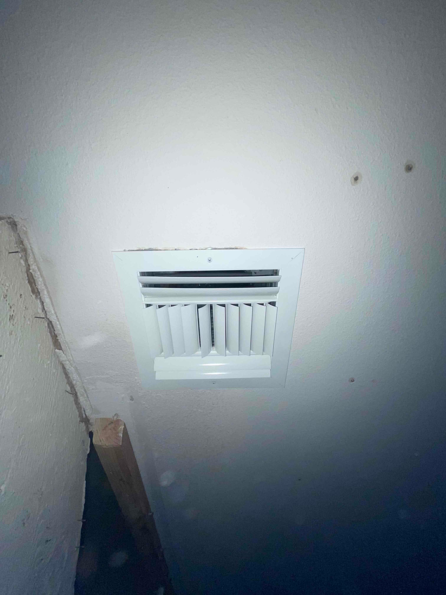 Ceiling supply register freshly installed with adjustable fins, secured with screws and trimmed flush to the drywall.