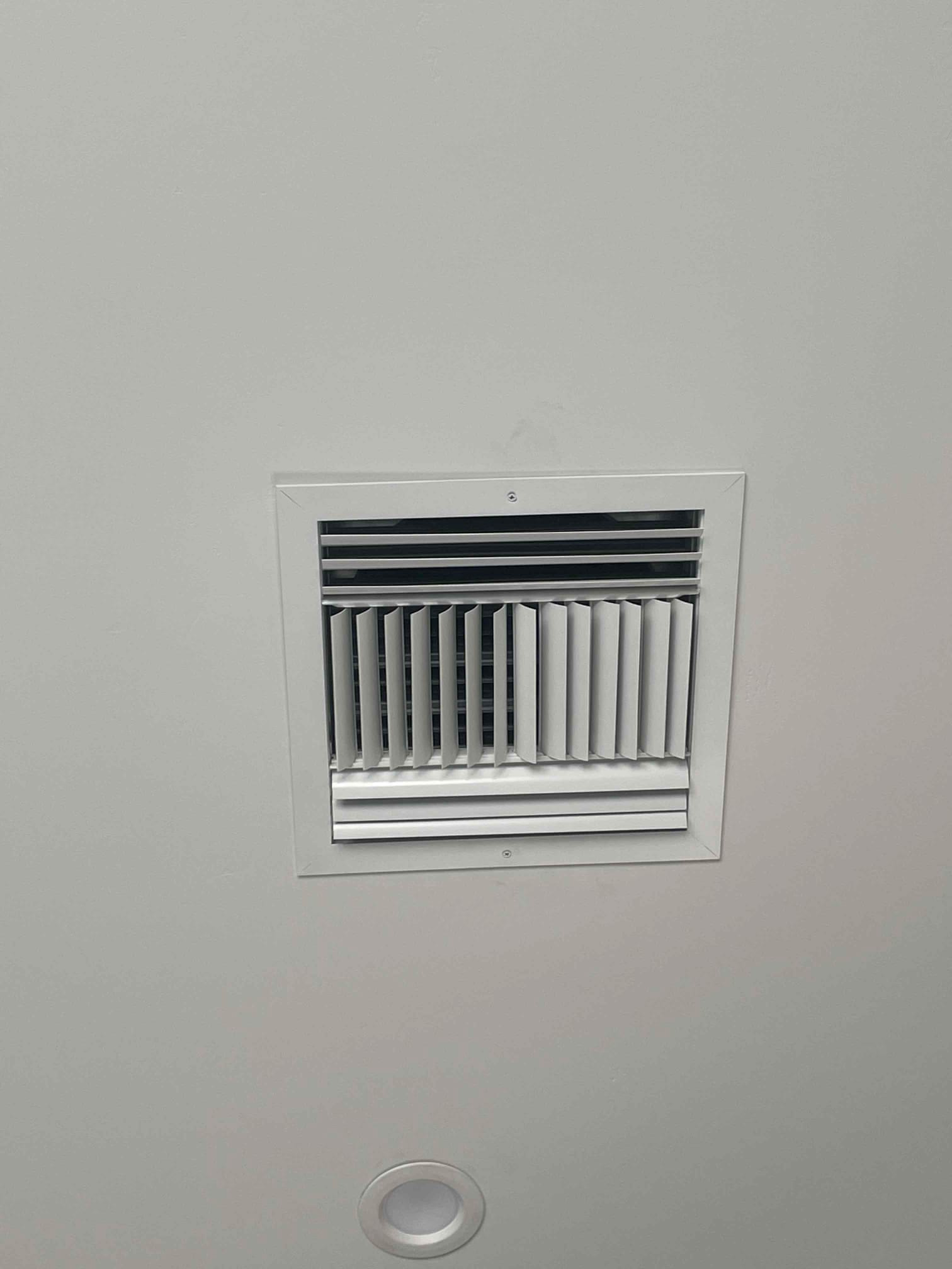 Ceiling supply register installed flush with the drywall, showing clean grille alignment beside a recessed light fixture.