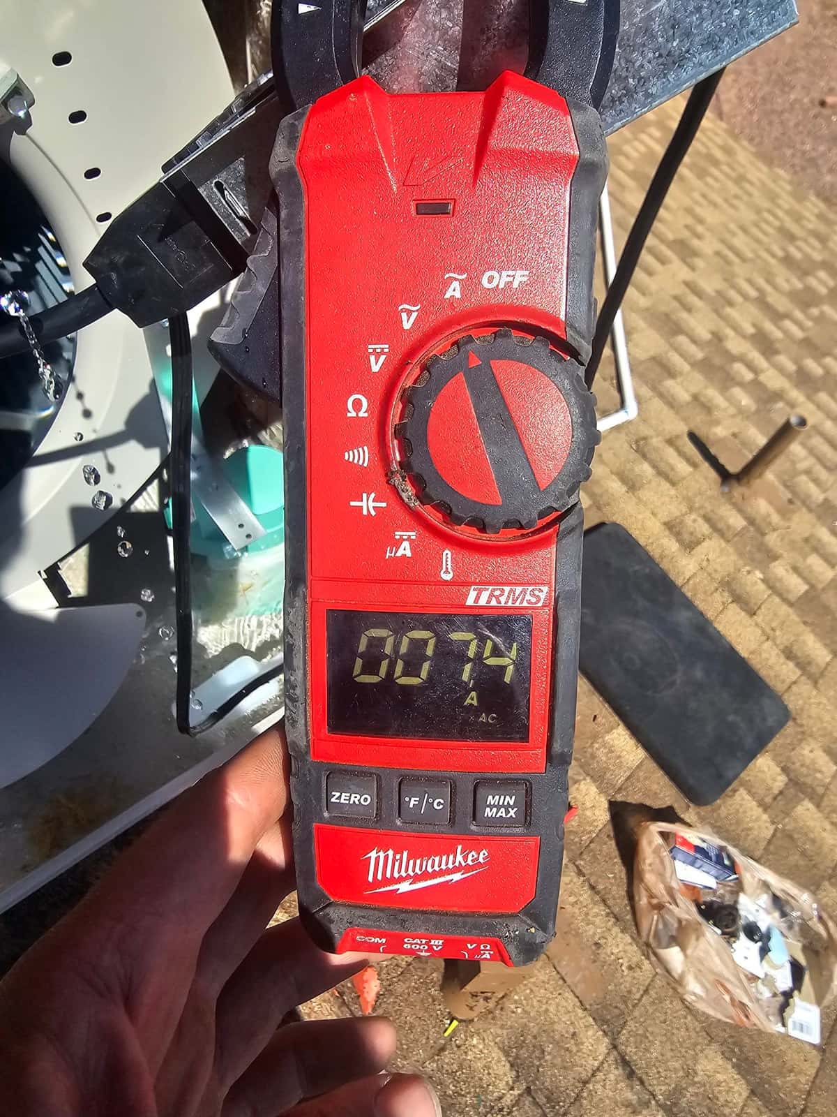Clamp meter measures AC current at the outdoor unit wiring, display showing 0.74 amps during electrical testing.
