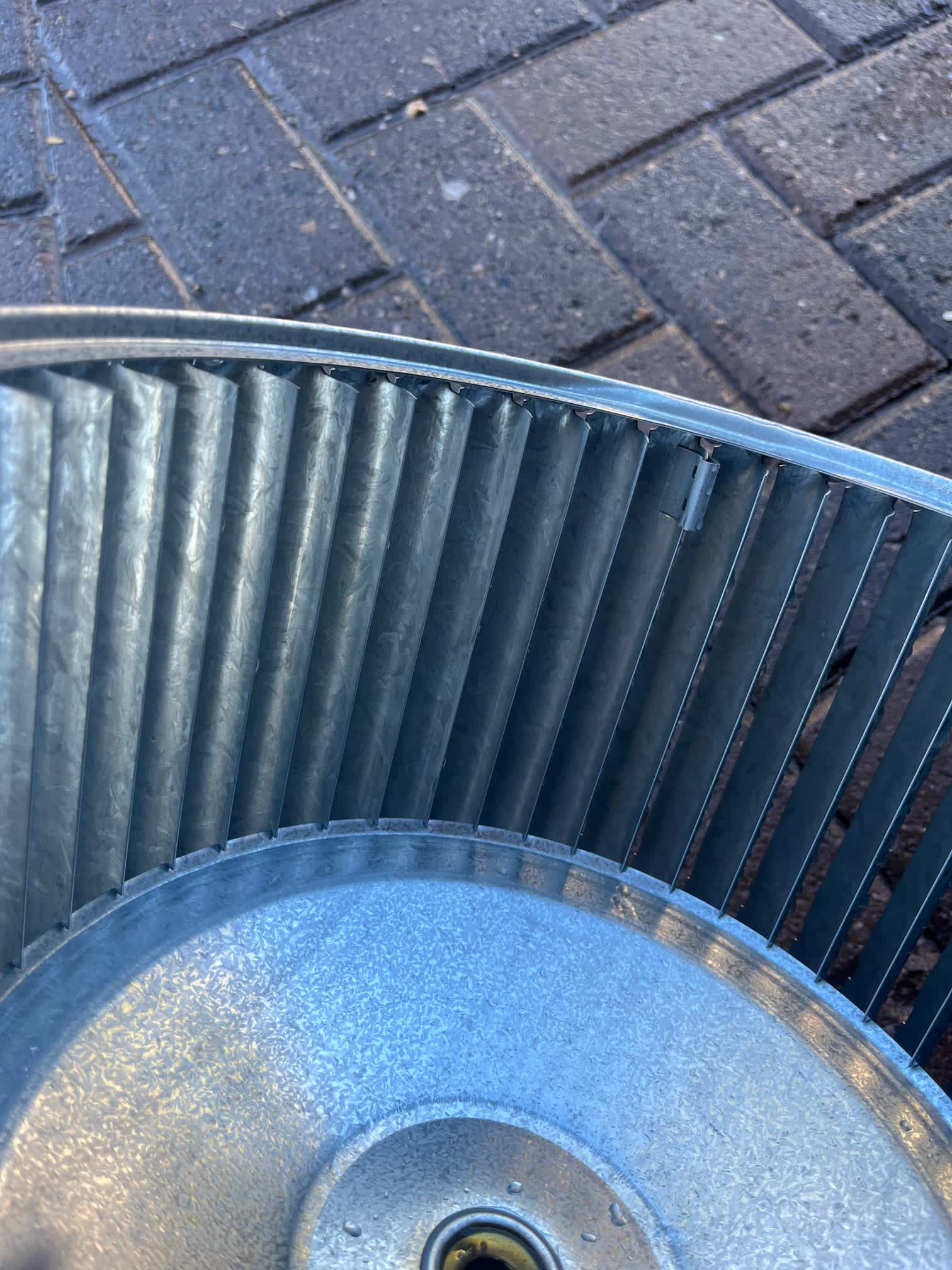 Close-up of a metal blower wheel removed from the air handler, showing clean blades and hub area.