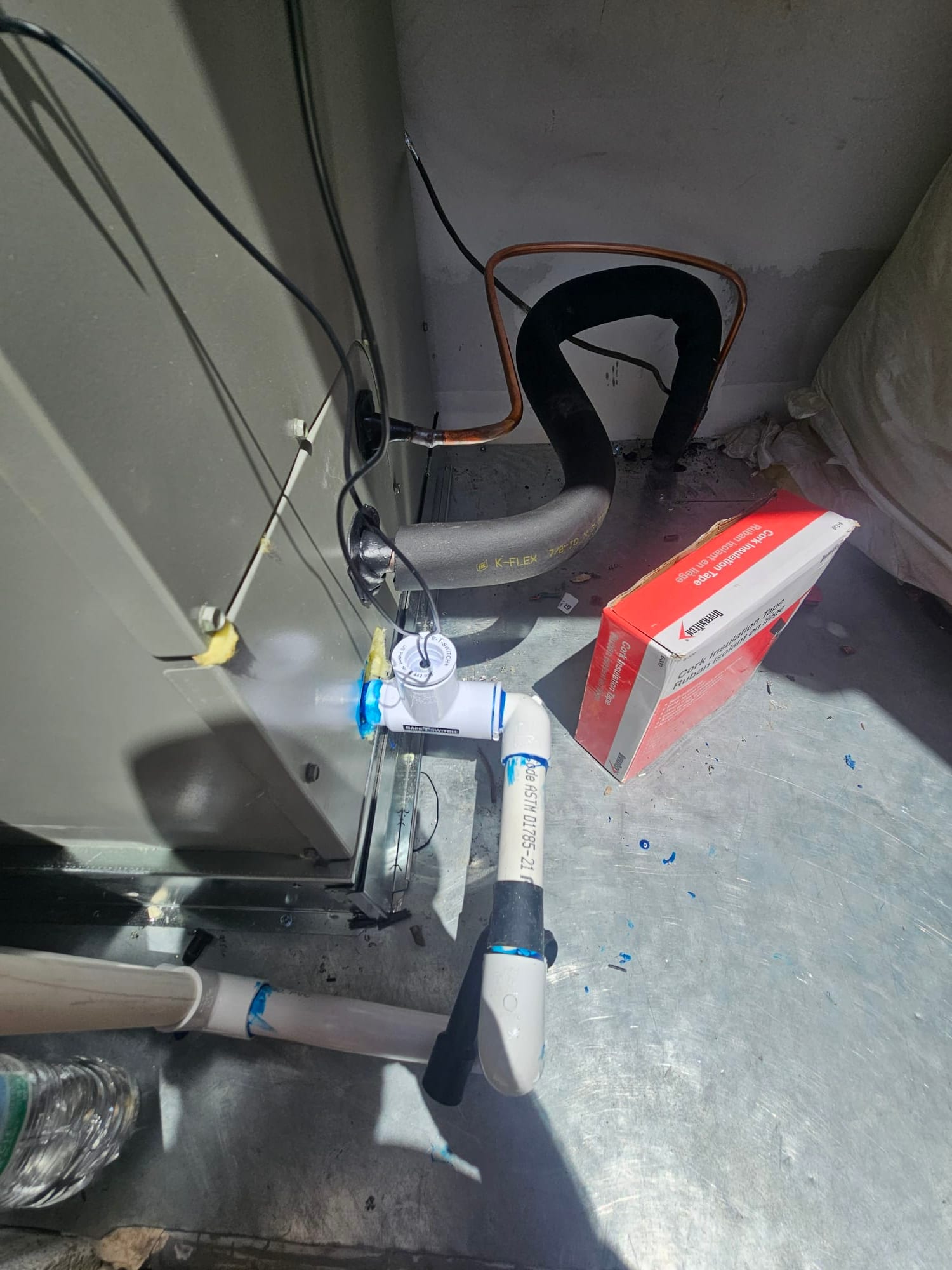 Condensate drain with cleanout and float switch installed at the air handler, alongside insulated refrigerant lines and copper tubing.