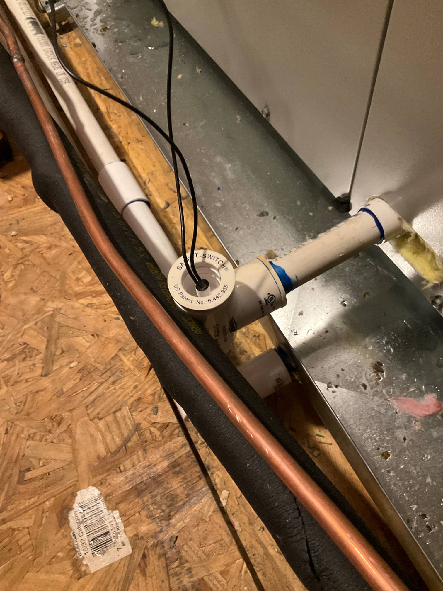 Condensate drain with float safety switch wired in, alongside insulated refrigerant line and copper tubing at the air handler.