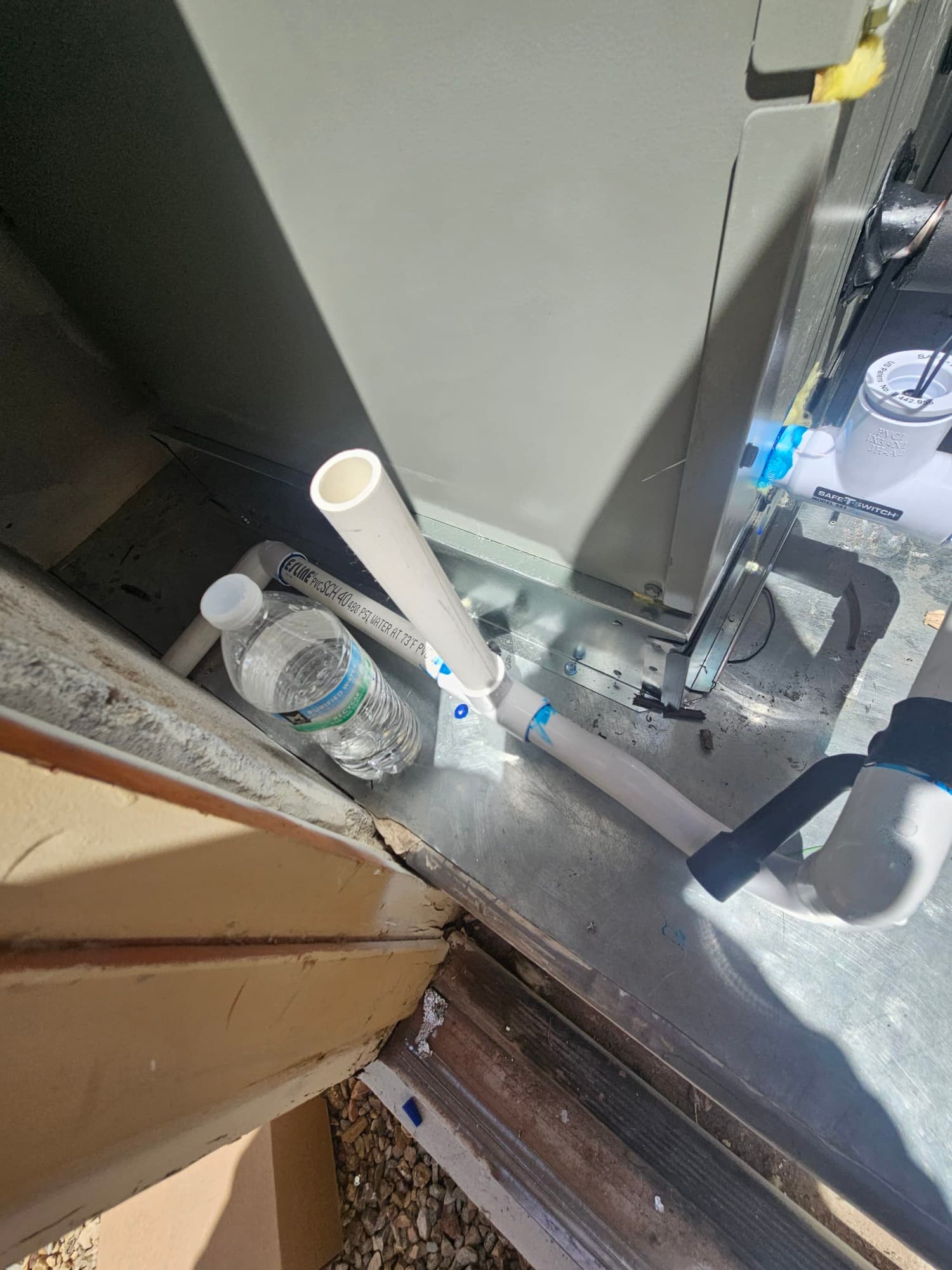 Condensate drain piping connected to the air handler with cleanout and trap, set on a metal pan near the doorway.