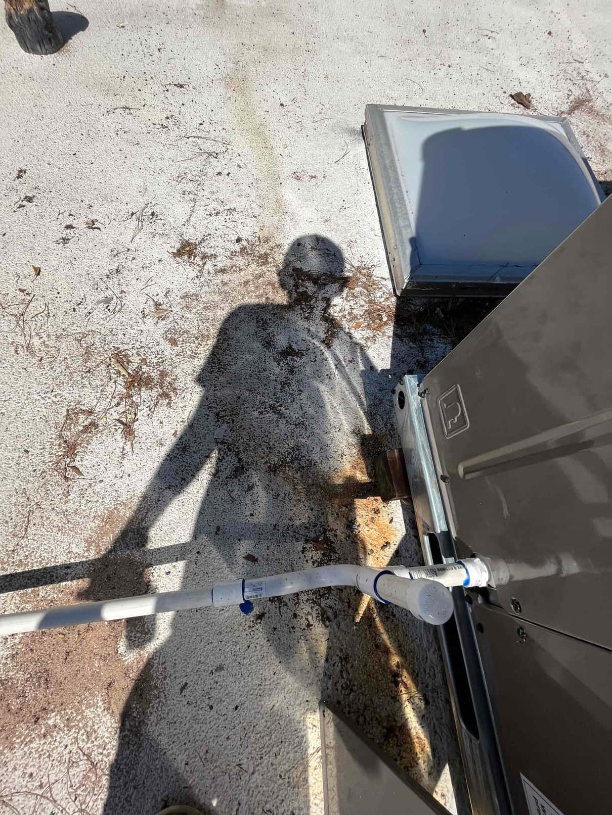 Condensate drain piping connected to the side of a rooftop package unit, secured with straps and cleanout cap installed.