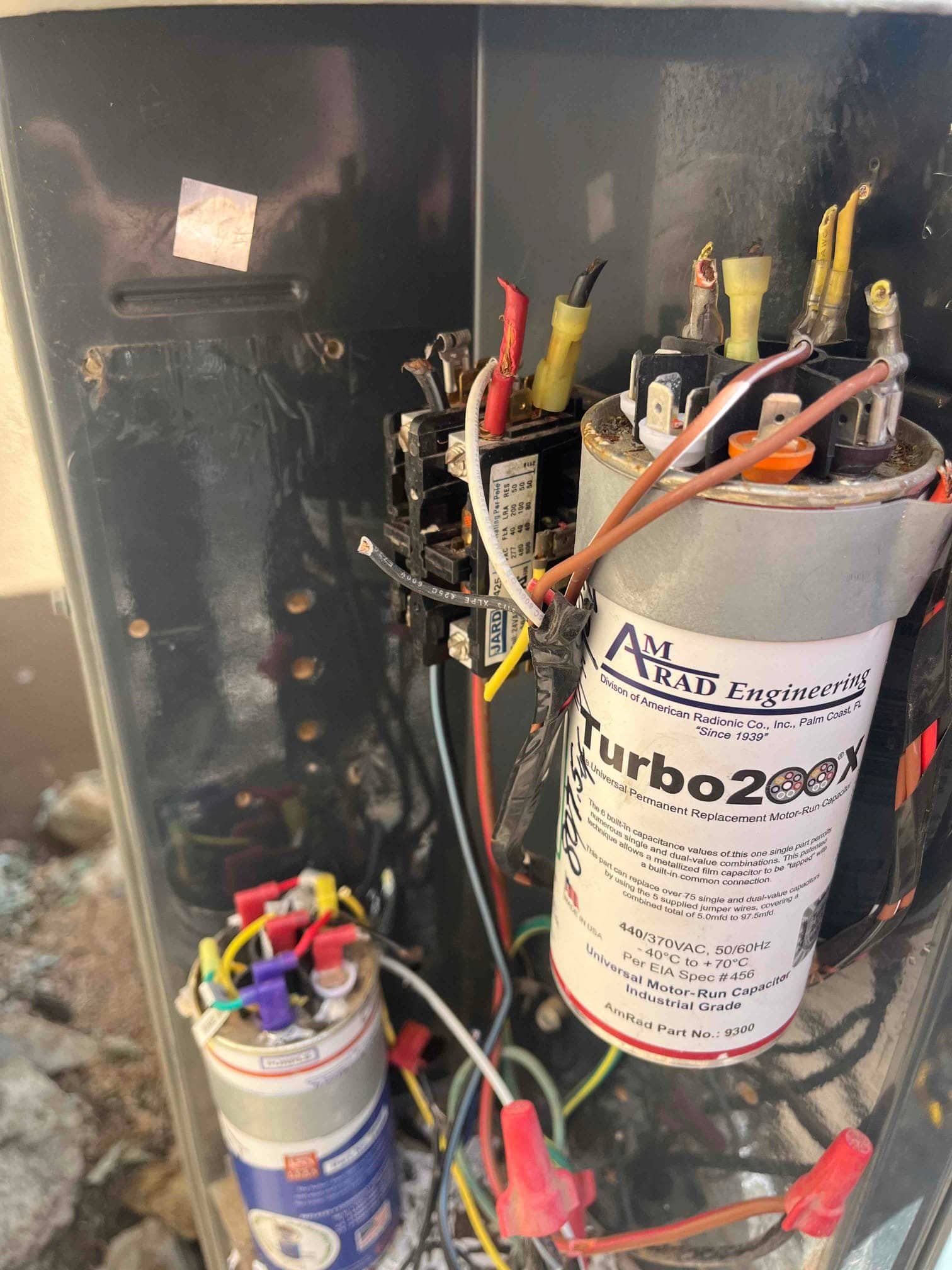 Condenser control compartment showing contactor, dual capacitors, wire connections, and wire nuts during electrical setup and verification.