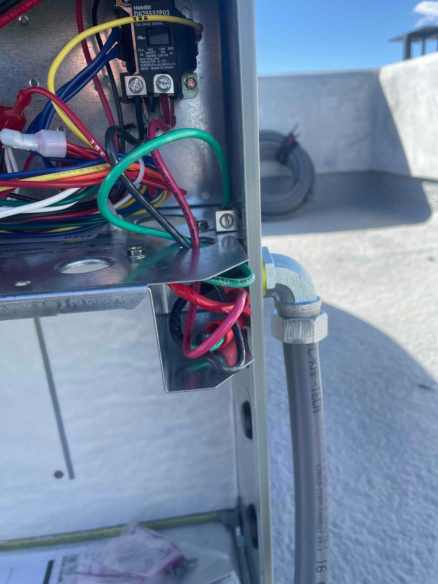 Control compartment wiring inside an outdoor HVAC unit with conduit connection and low-voltage and line-voltage conductors neatly routed.