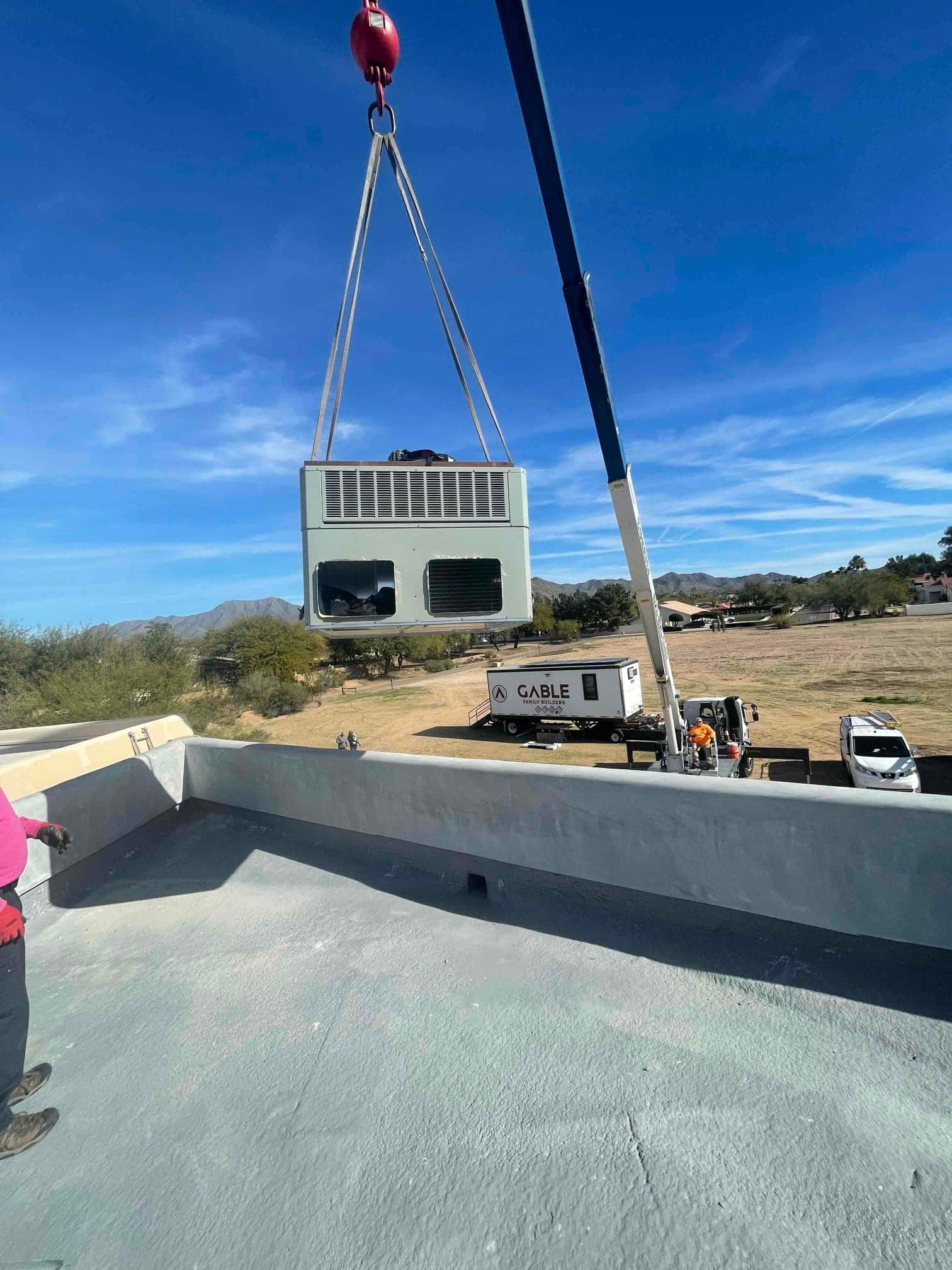 Crane lifts a rooftop HVAC package unit into position during installation, with rigging straps attached and crew coordinating below.