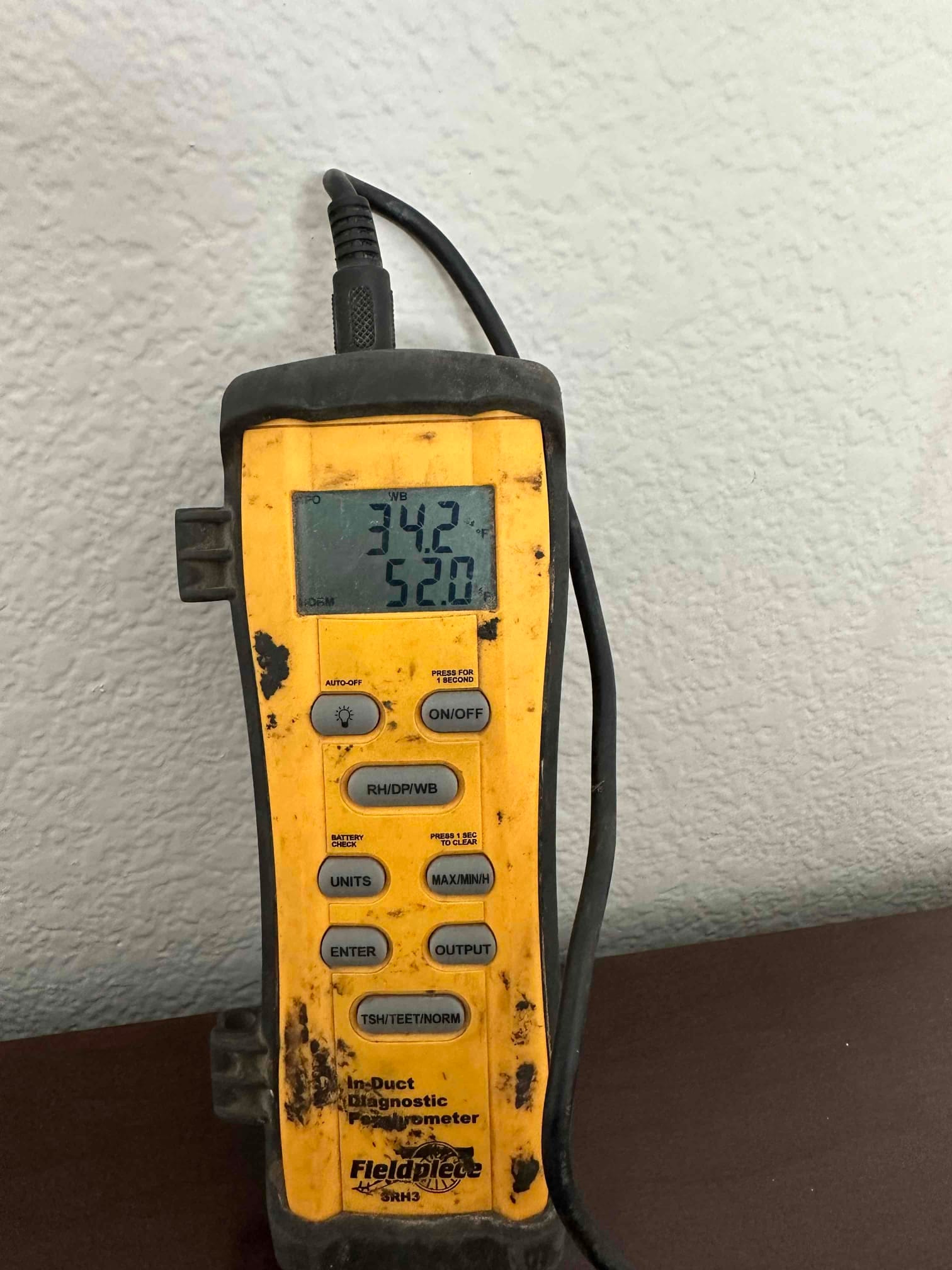 Digital hygrometer displays 52.0°F dry-bulb temperature during air-side commissioning after installing the new system.