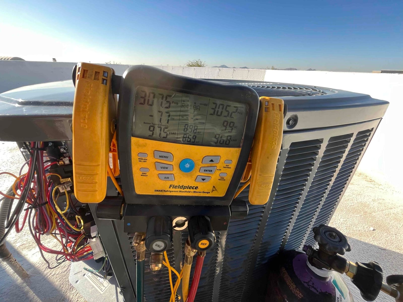 Digital manifold connected to an outdoor unit shows operating suction and liquid pressures while the system runs during commissioning.