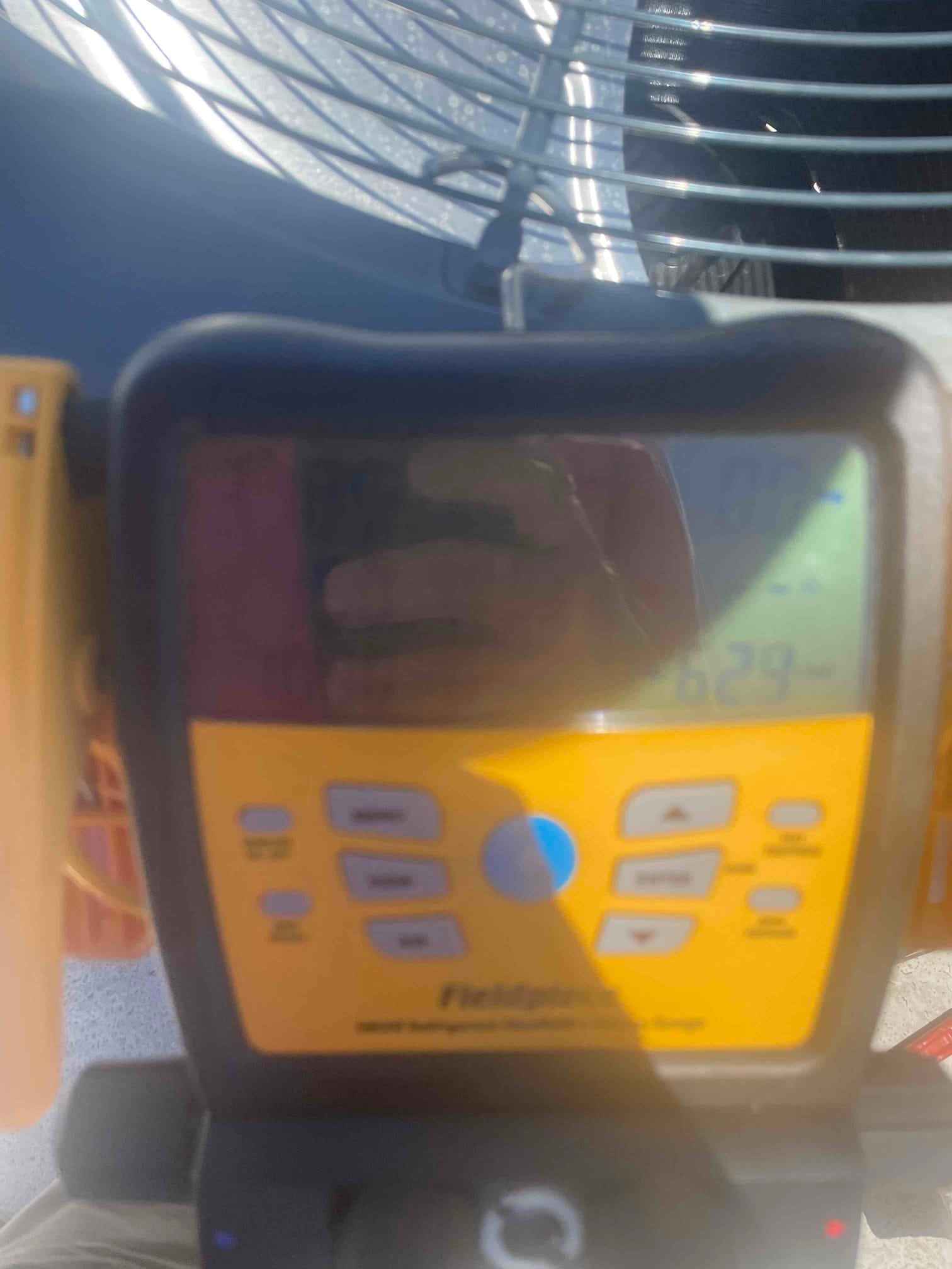 Digital manifold gauge attached at the outdoor condenser, screen obscured by glare and unreadable in bright sunlight.