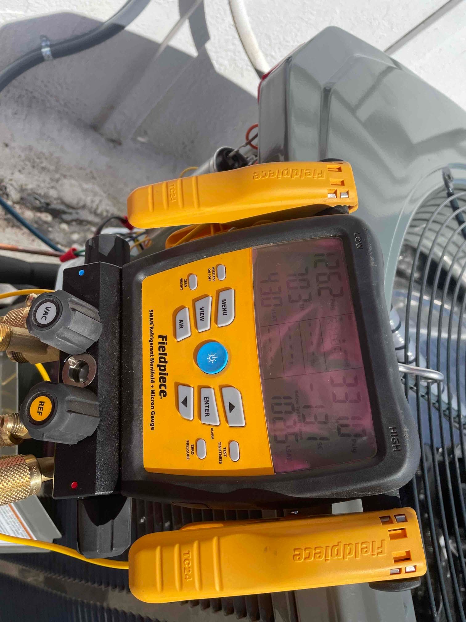Digital manifold gauges connected to the outdoor unit display different high and low pressures during system operation for commissioning checks.