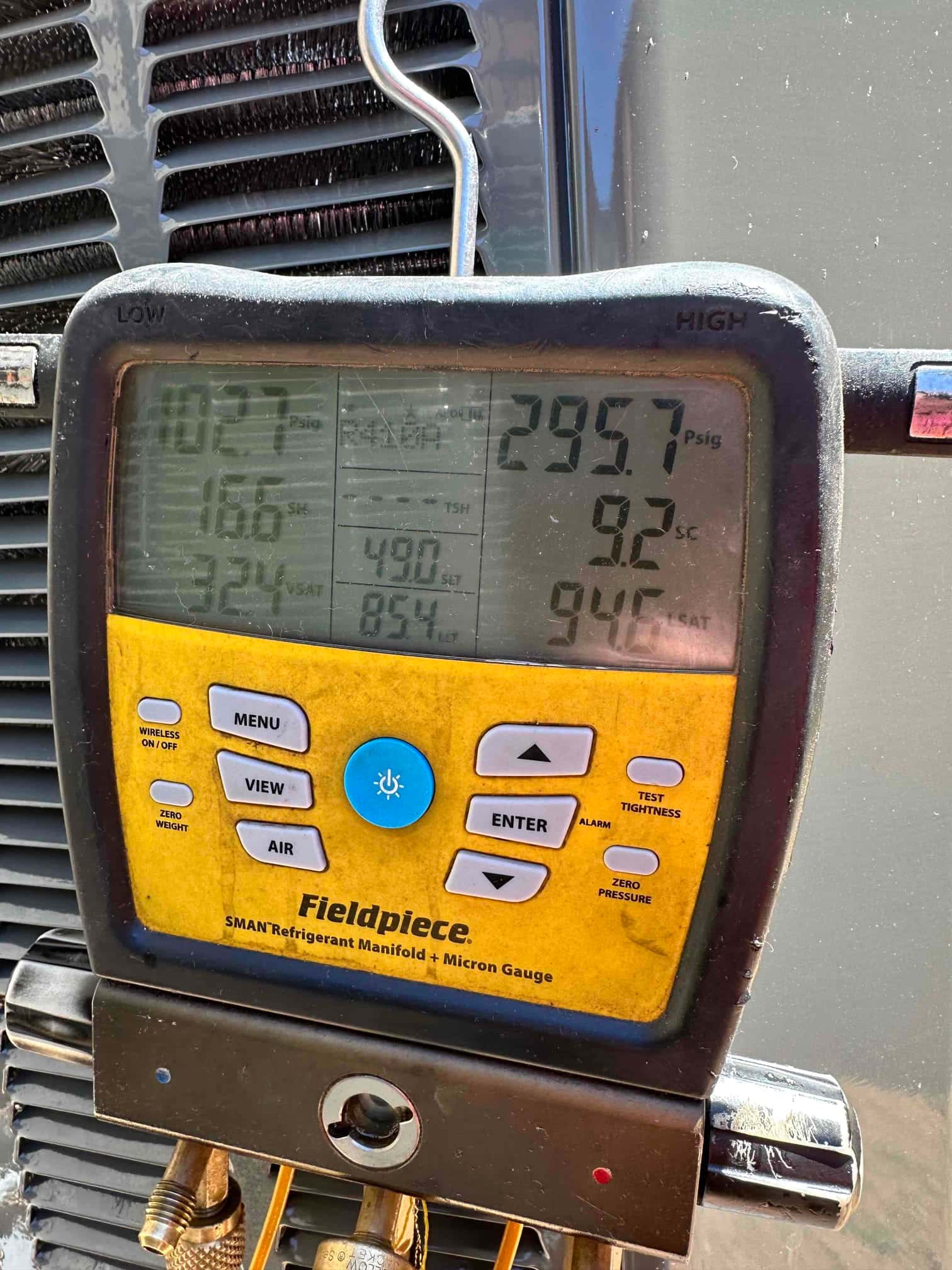 Digital manifold shows operating pressures on an outdoor condenser during commissioning, with distinct low and high side readings and subcooling displayed.