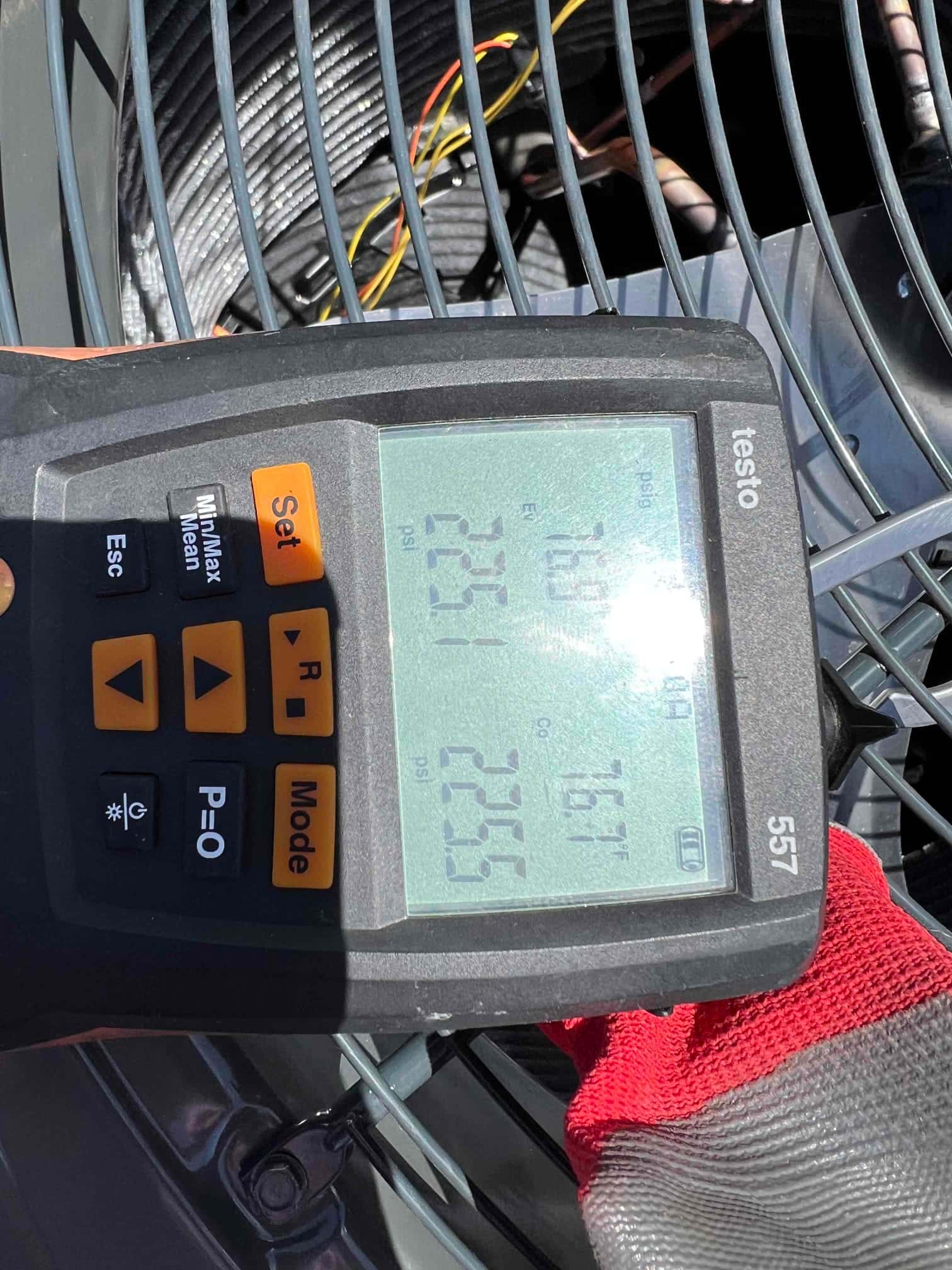 Digital manifold shows system operating pressures with distinct high and low sides while the outdoor condenser fan guard is visible below.