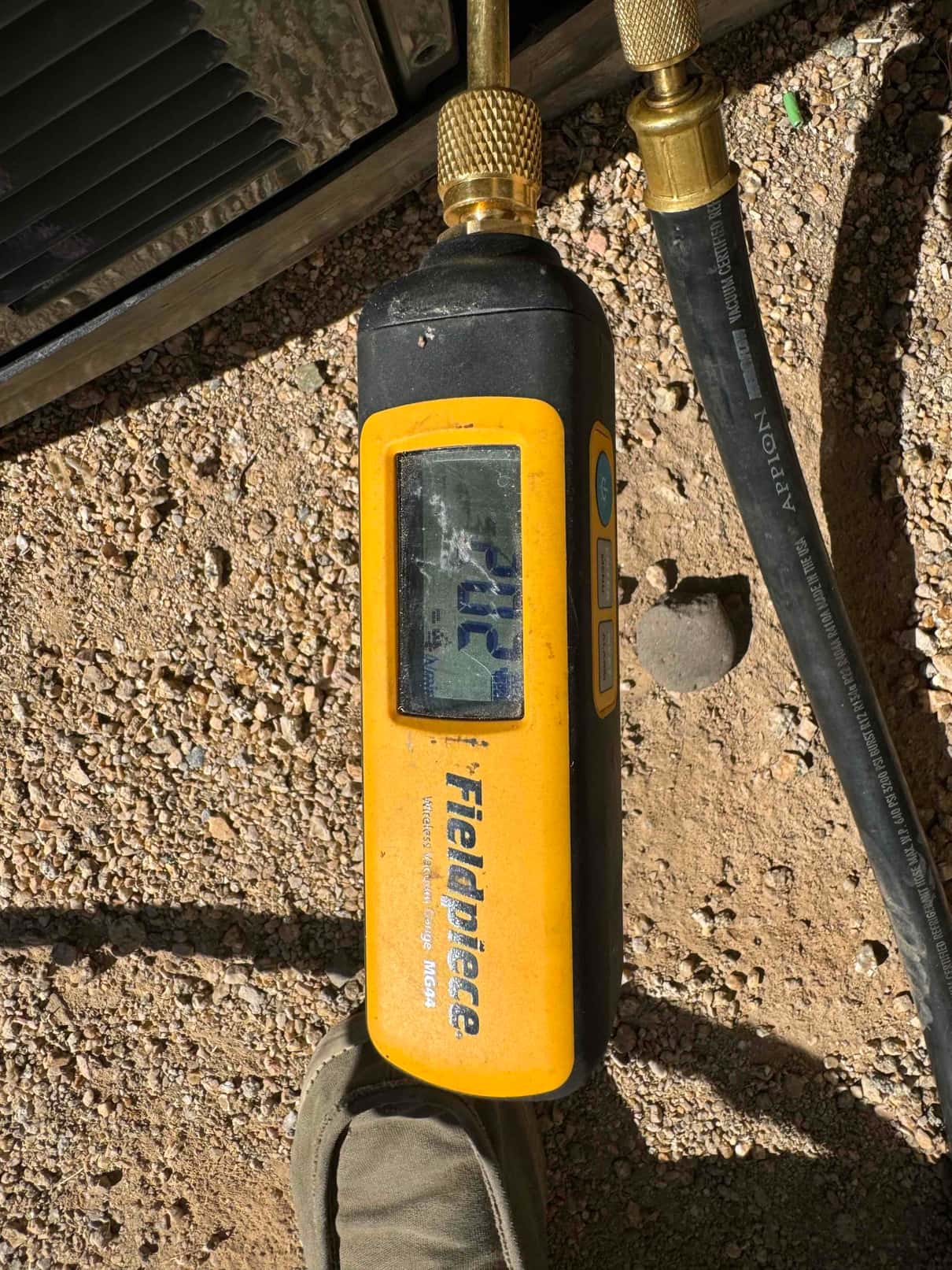 Digital micron gauge connected to a vacuum hose shows 172 microns during system evacuation prior to refrigerant charging.
