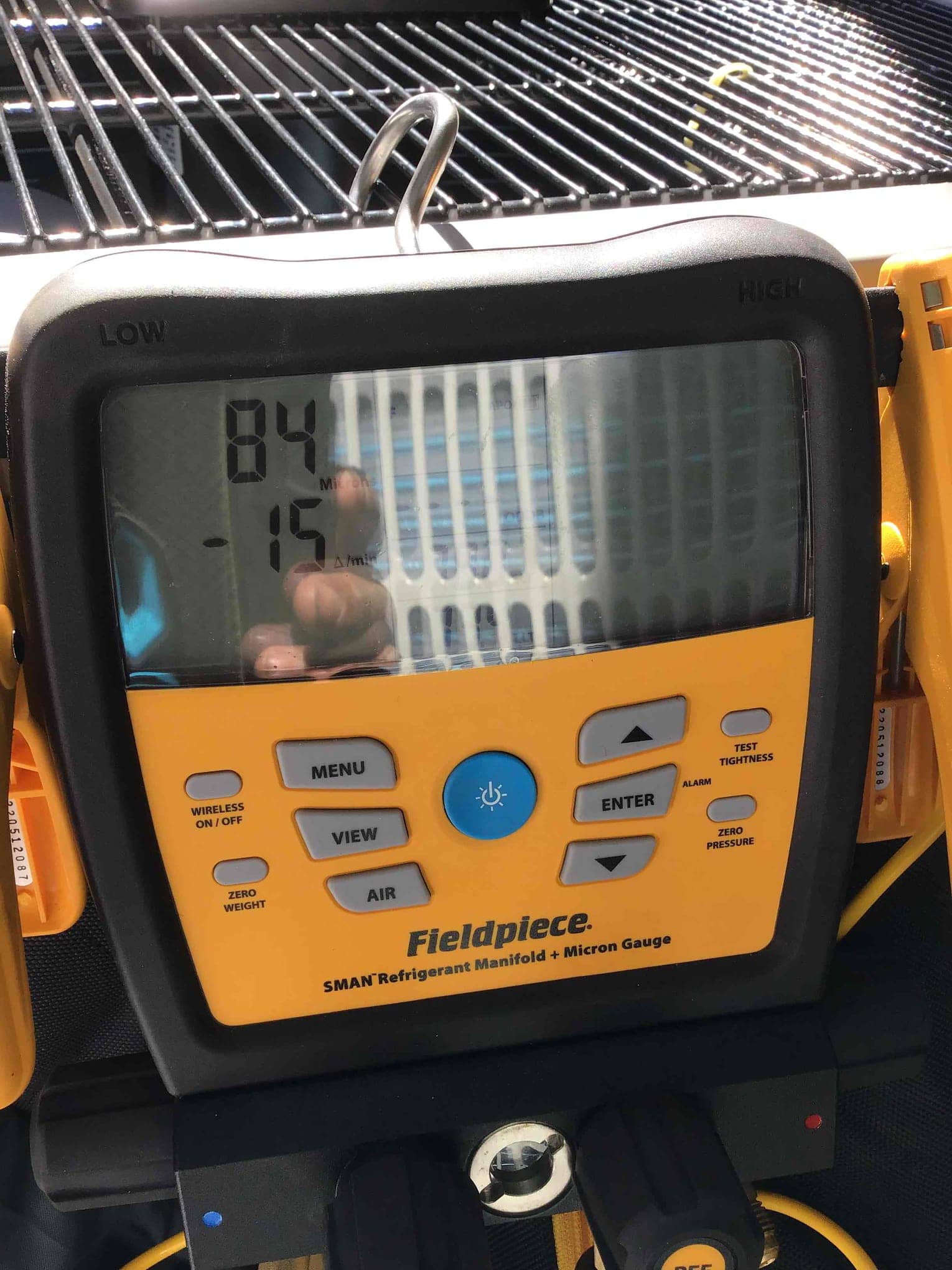 Digital refrigerant manifold screen displays an 84 reading with -15 beneath, attached at an outdoor condensing unit.