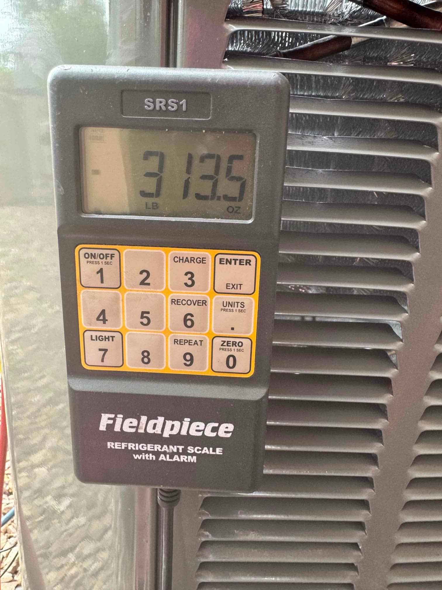 Digital refrigerant scale displays 3 pounds 13.5 ounces during charging beside the outdoor condenser cabinet.