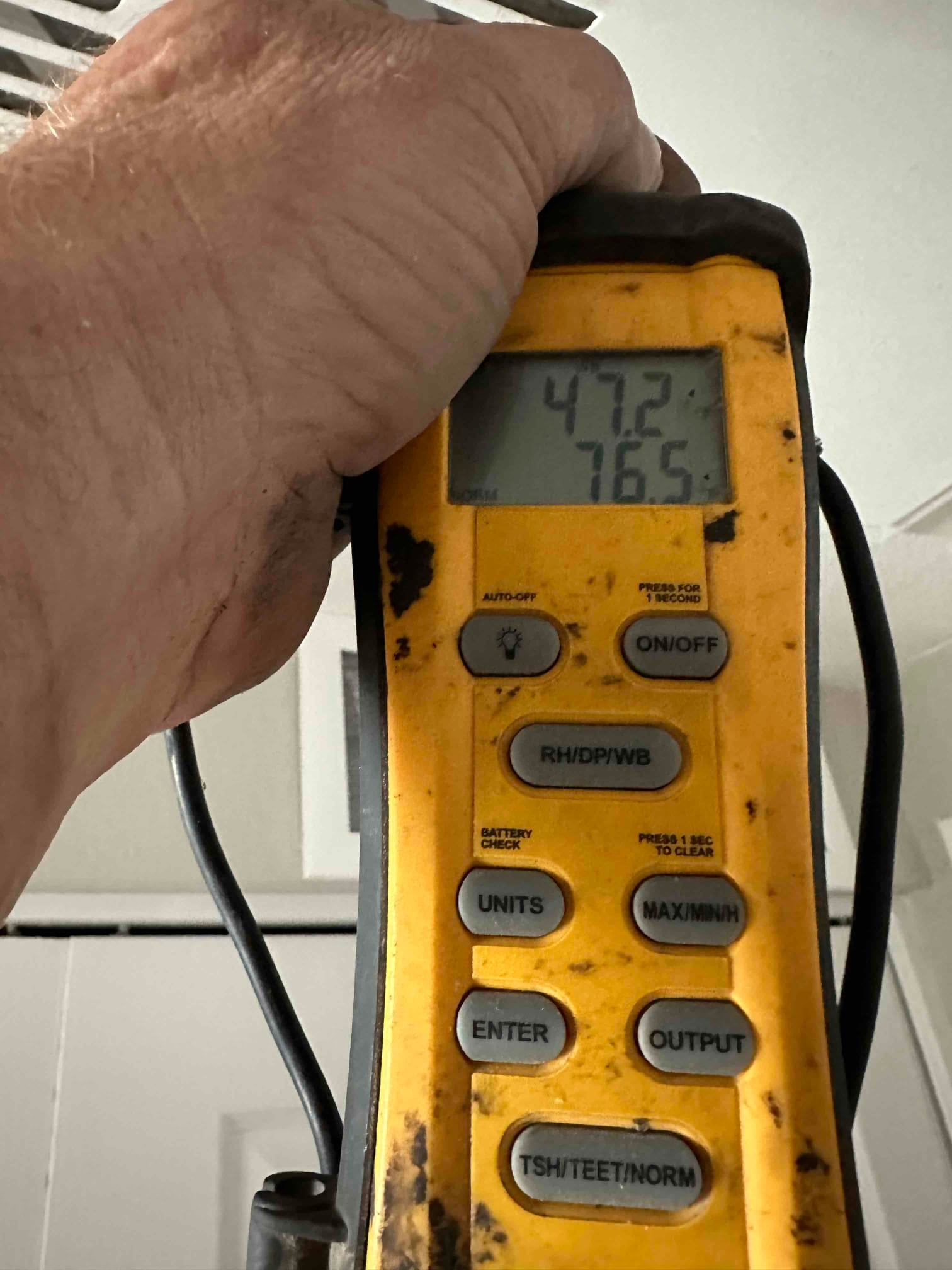 Digital thermometer held at a ceiling register shows 47.2°F supply air temperature with a secondary display reading 76.5.