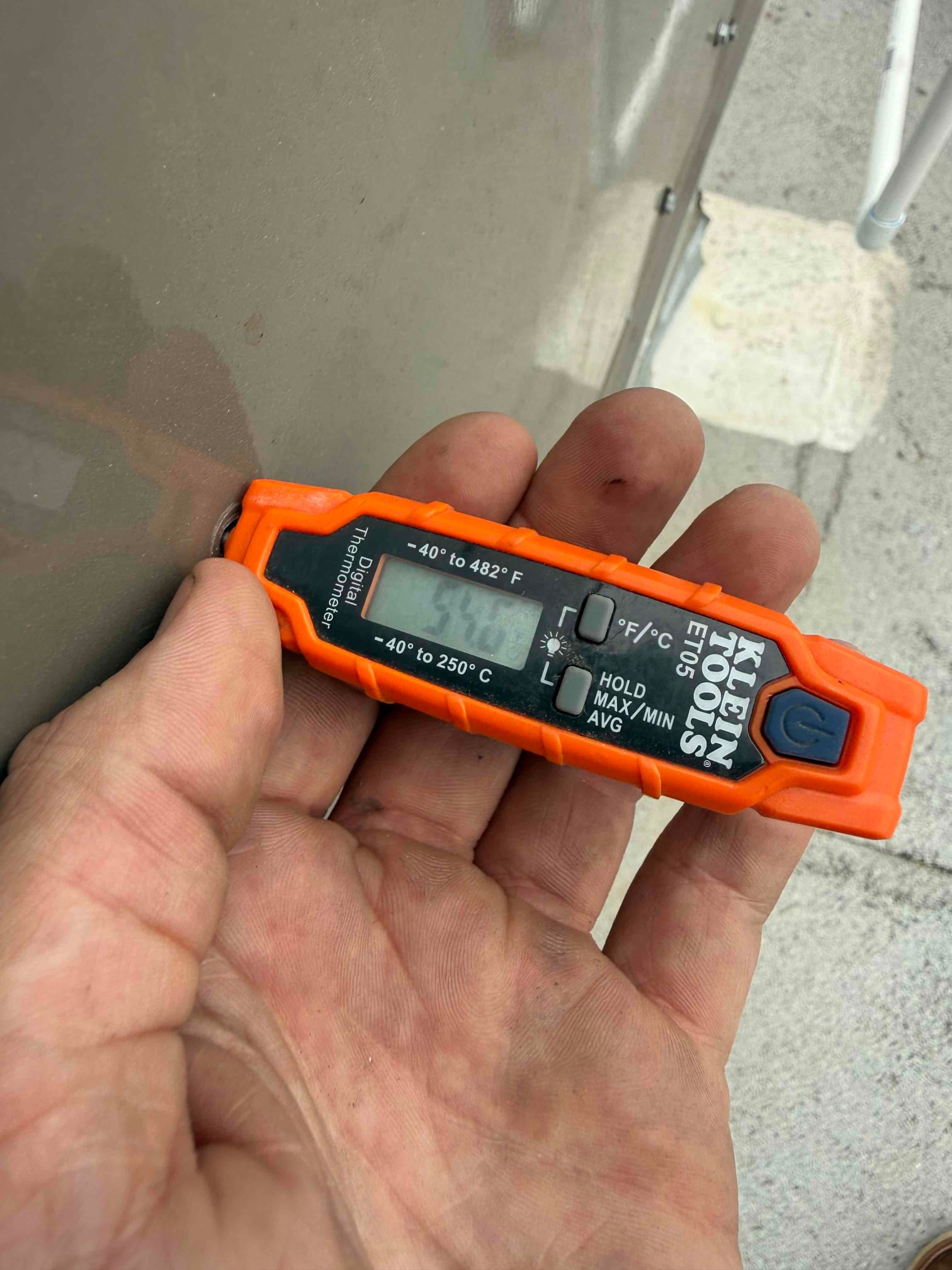 Digital thermometer held at the unit reads 54°F, documenting supply air temperature during commissioning.