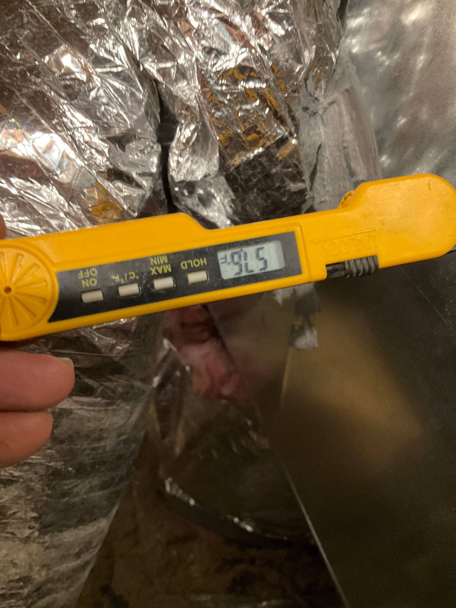 Digital thermometer inserted at a metal duct shows 57.6°F, documenting cool supply air temperature after system start-up.
