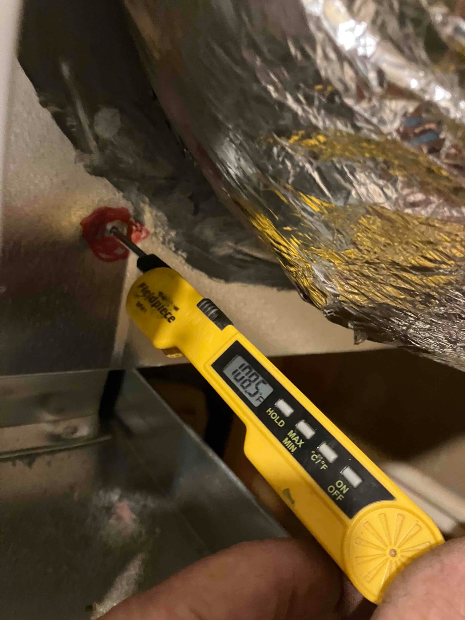 Digital thermometer probe inserted into duct measures air temperature at 60.5 degrees Fahrenheit during system airflow testing.