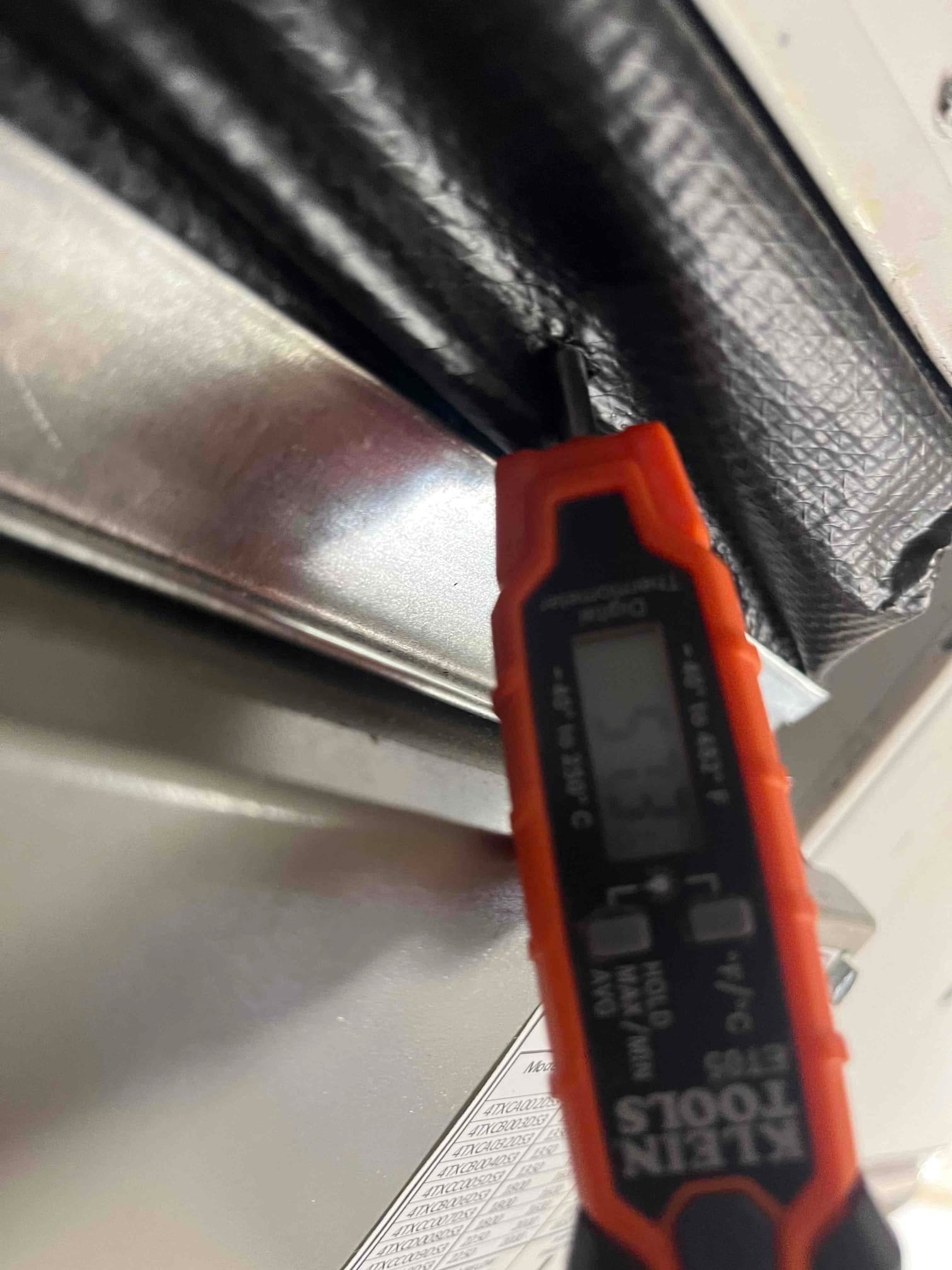 Digital thermometer probe inserted into supply plenum insulation shows 55°F, documenting cooled supply air temperature after startup.