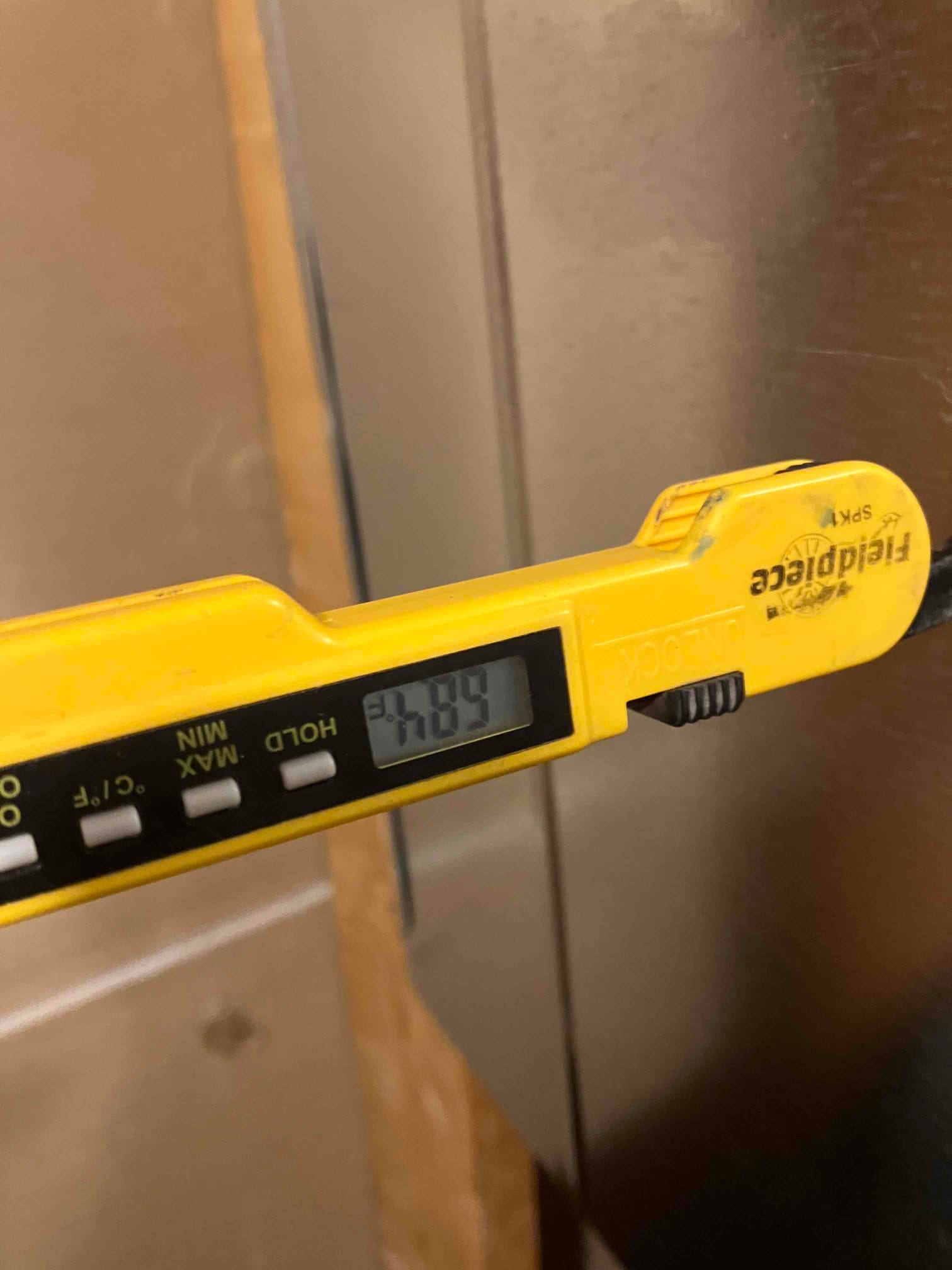 Digital thermometer probe measures air temperature at the duct, displaying 74.9 degrees Fahrenheit on the screen.