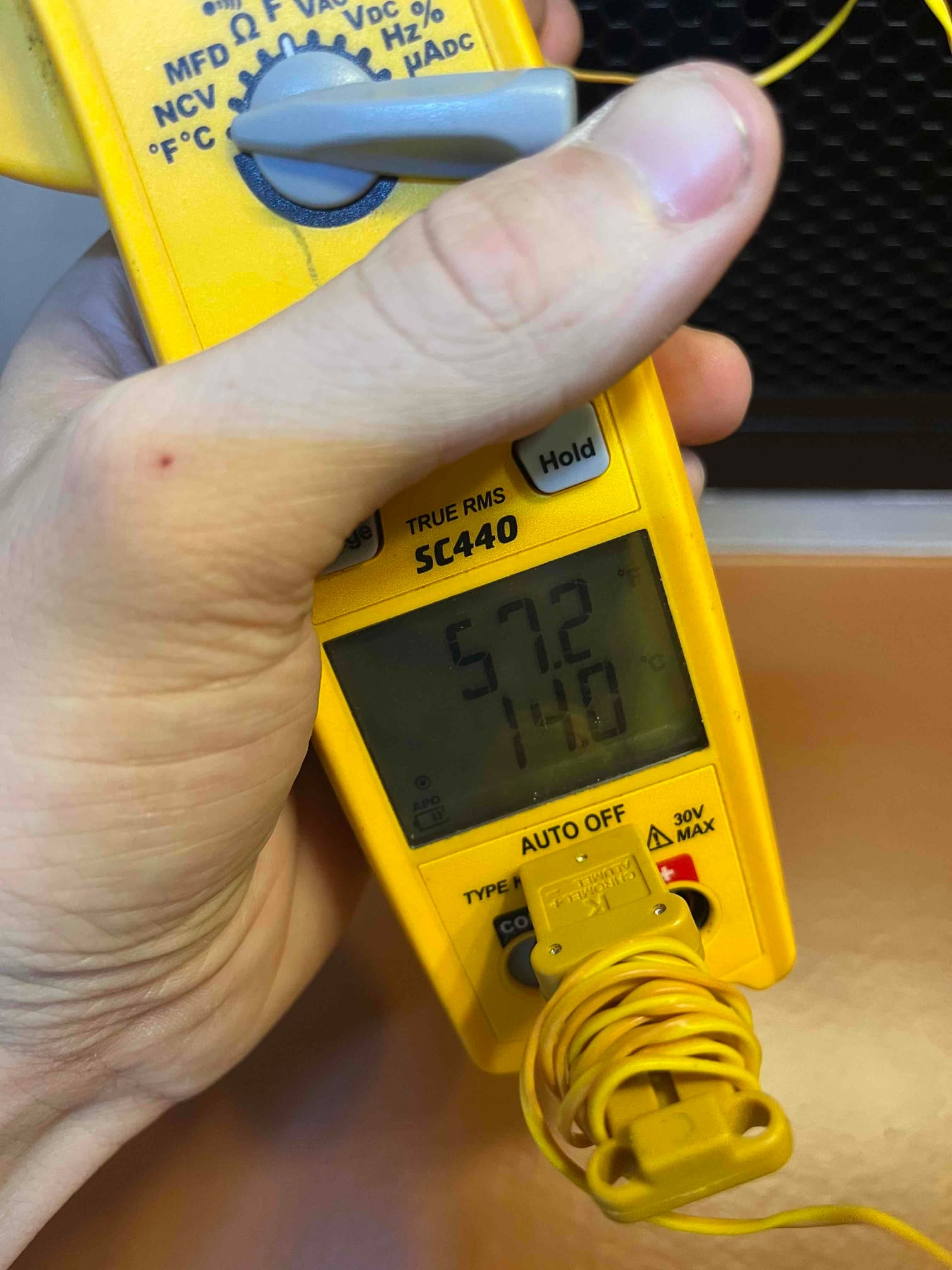 Digital thermometer probe shows 57.2 degrees Fahrenheit while measuring air temperature during system startup checks.