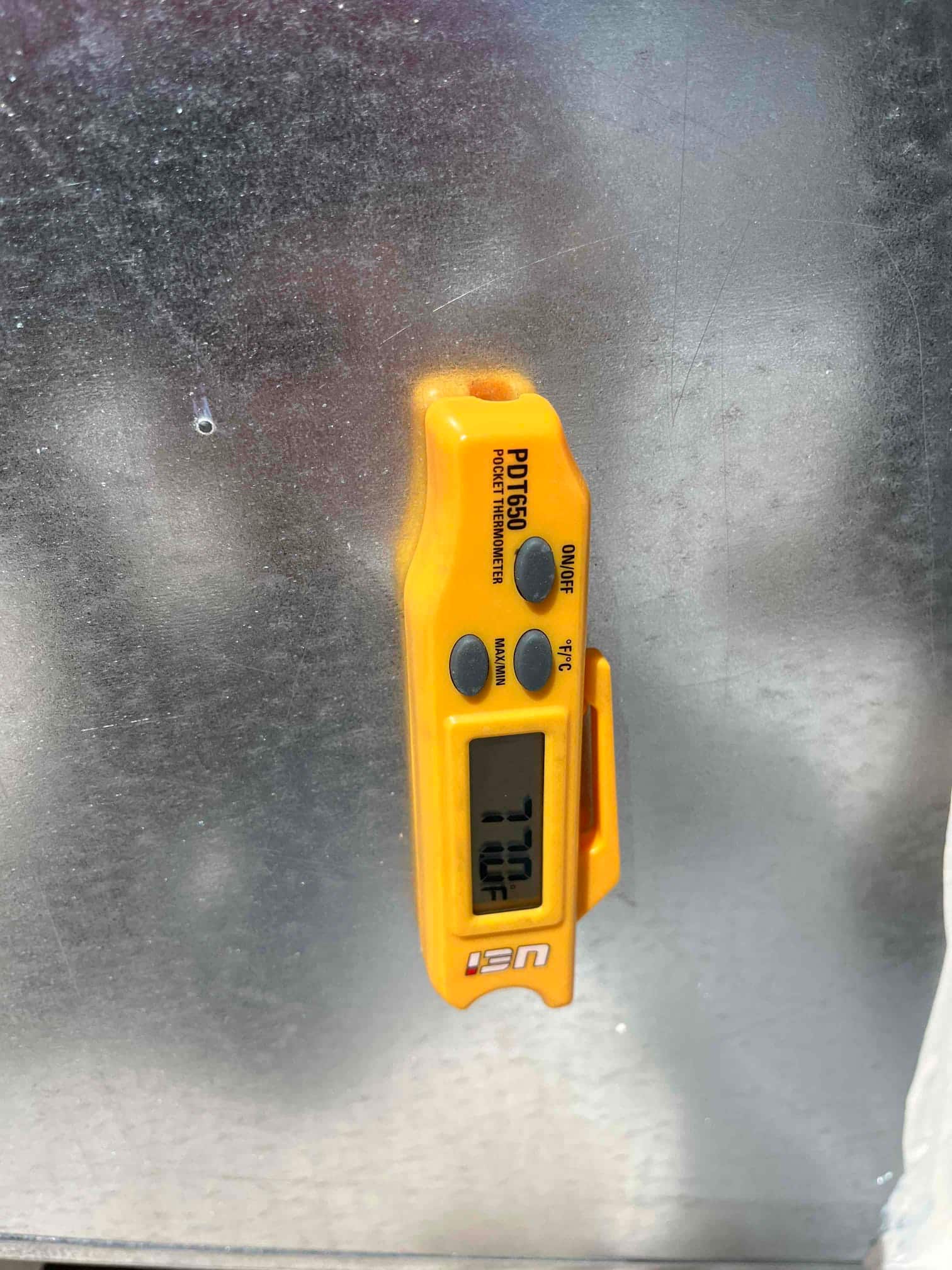 Digital thermometer reads 77.0°F on the duct surface, documenting return air temperature during commissioning.