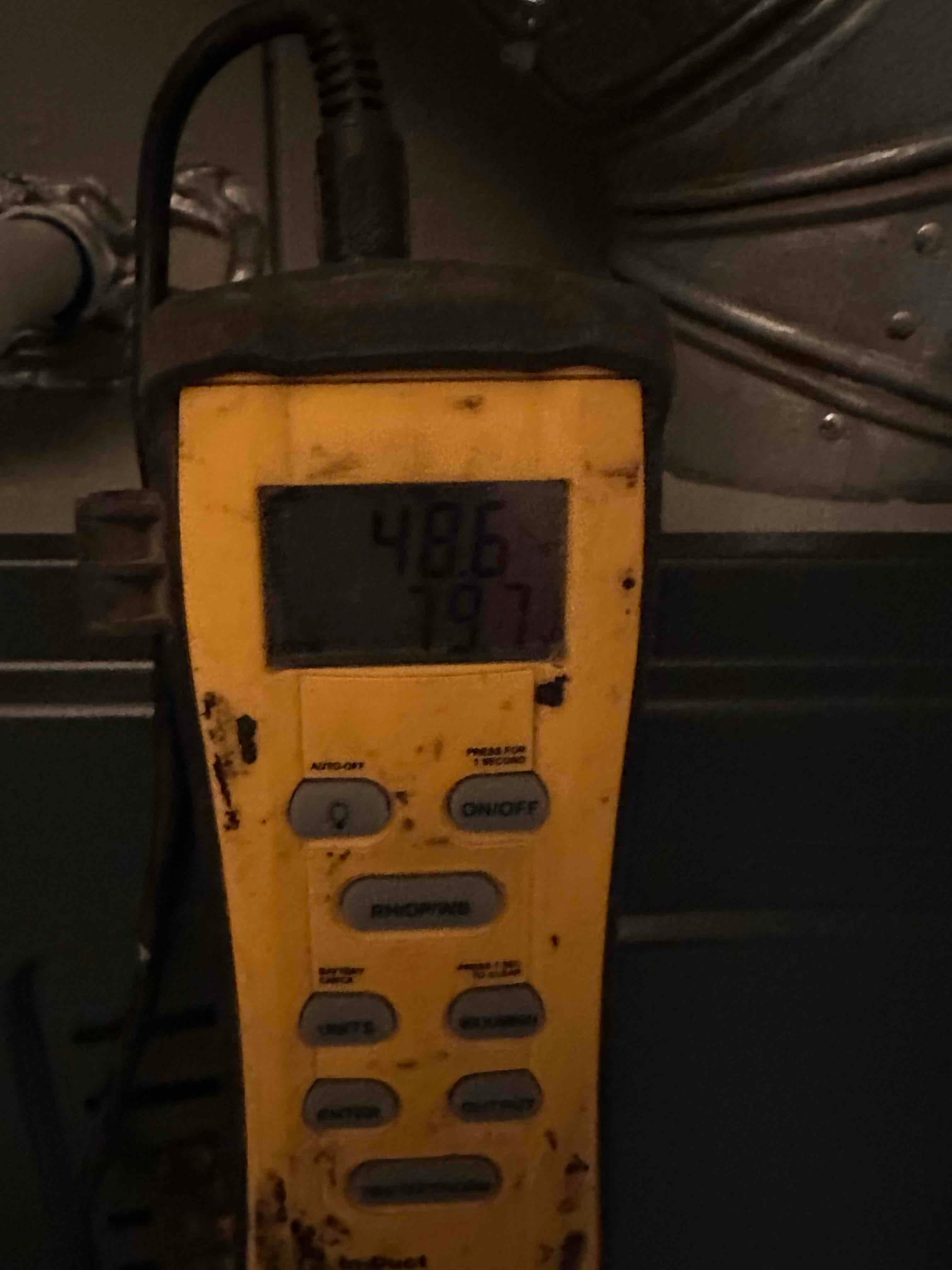 Digital thermometer shows a 48.6 degree reading while measuring air temperature near the indoor unit.