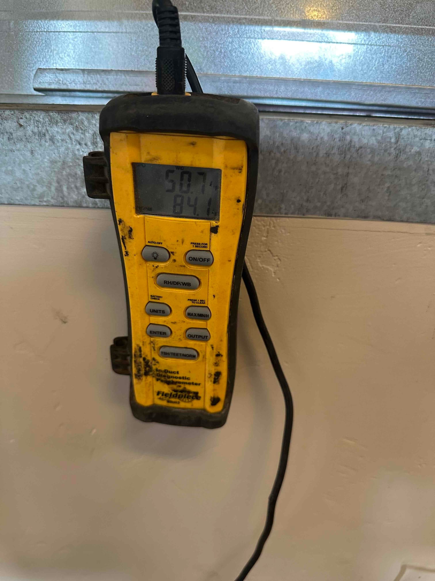 Digital thermometer shows 50.7 degrees on the supply duct, documenting cooled air temperature during commissioning.