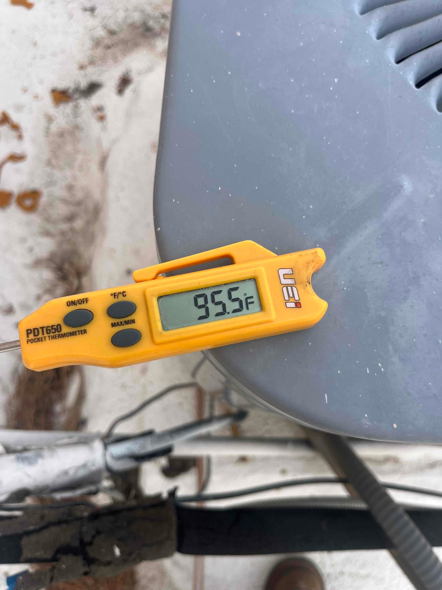 Digital thermometer shows 95.5 °F on the outdoor condenser unit’s top surface during air conditioning repair.