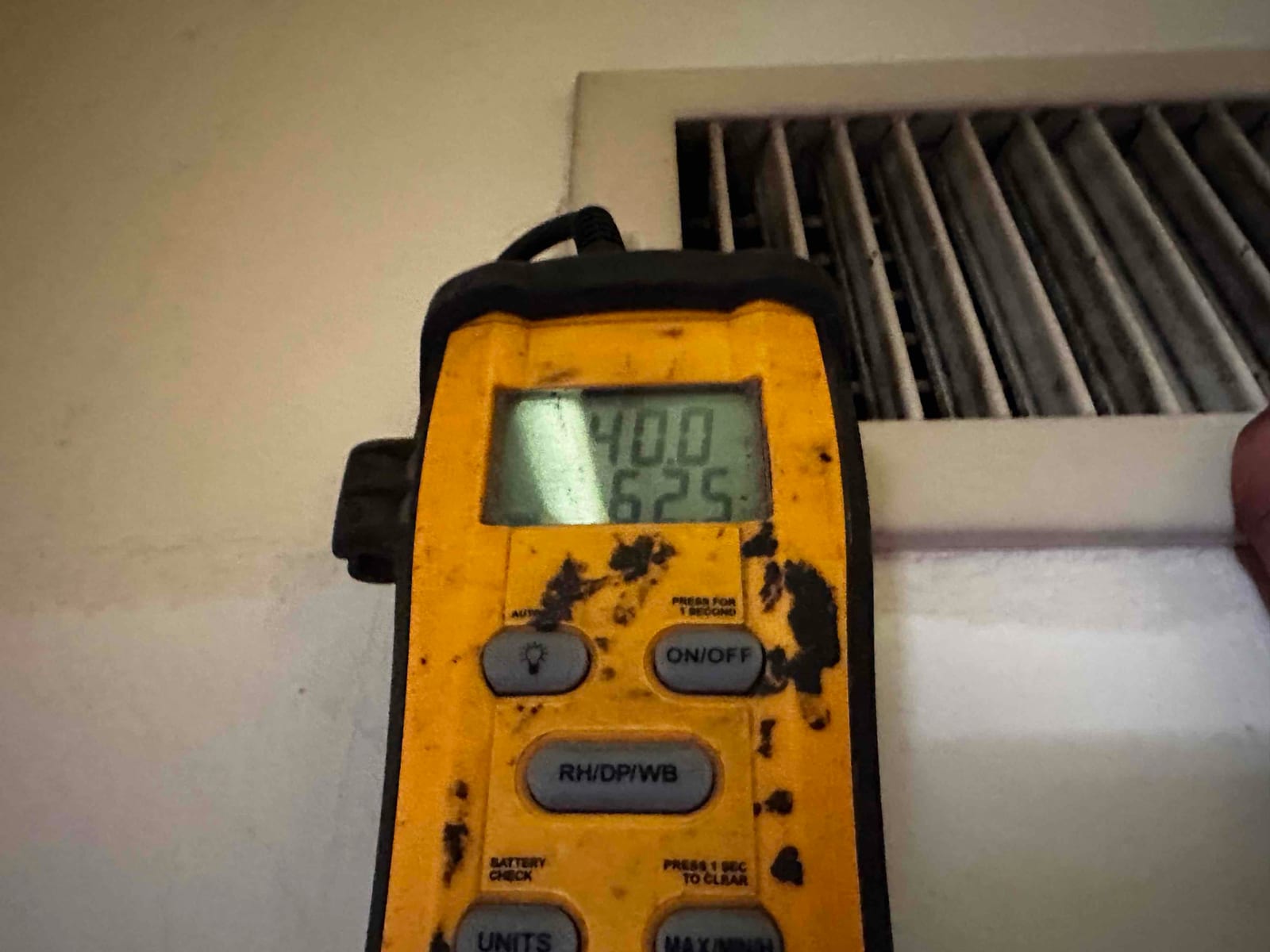 Digital thermometer at a supply register shows cooled air temperature for system air-side commissioning.