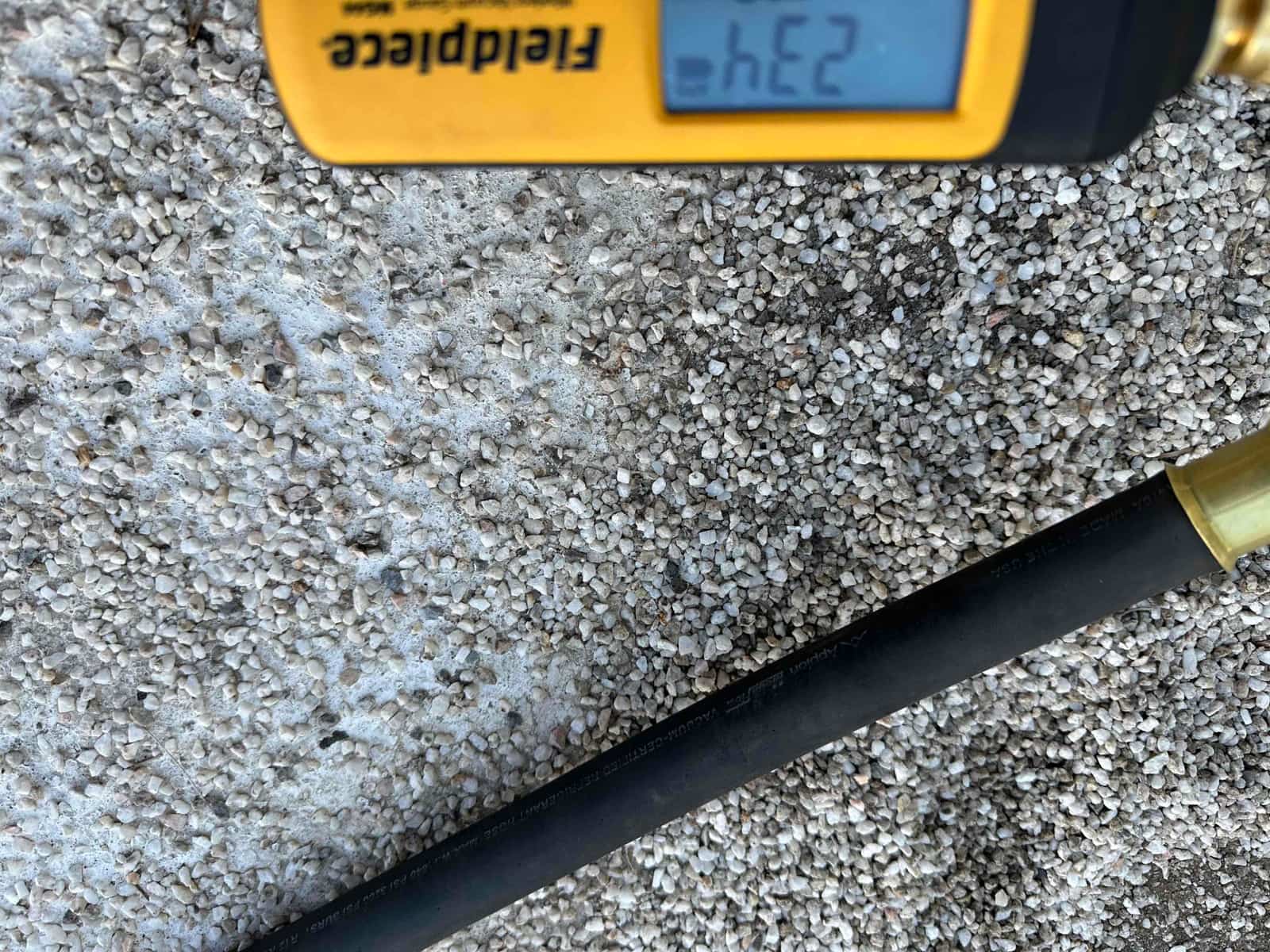 Digital vacuum gauge connected to a hose displays the micron level during system evacuation before refrigerant charging.