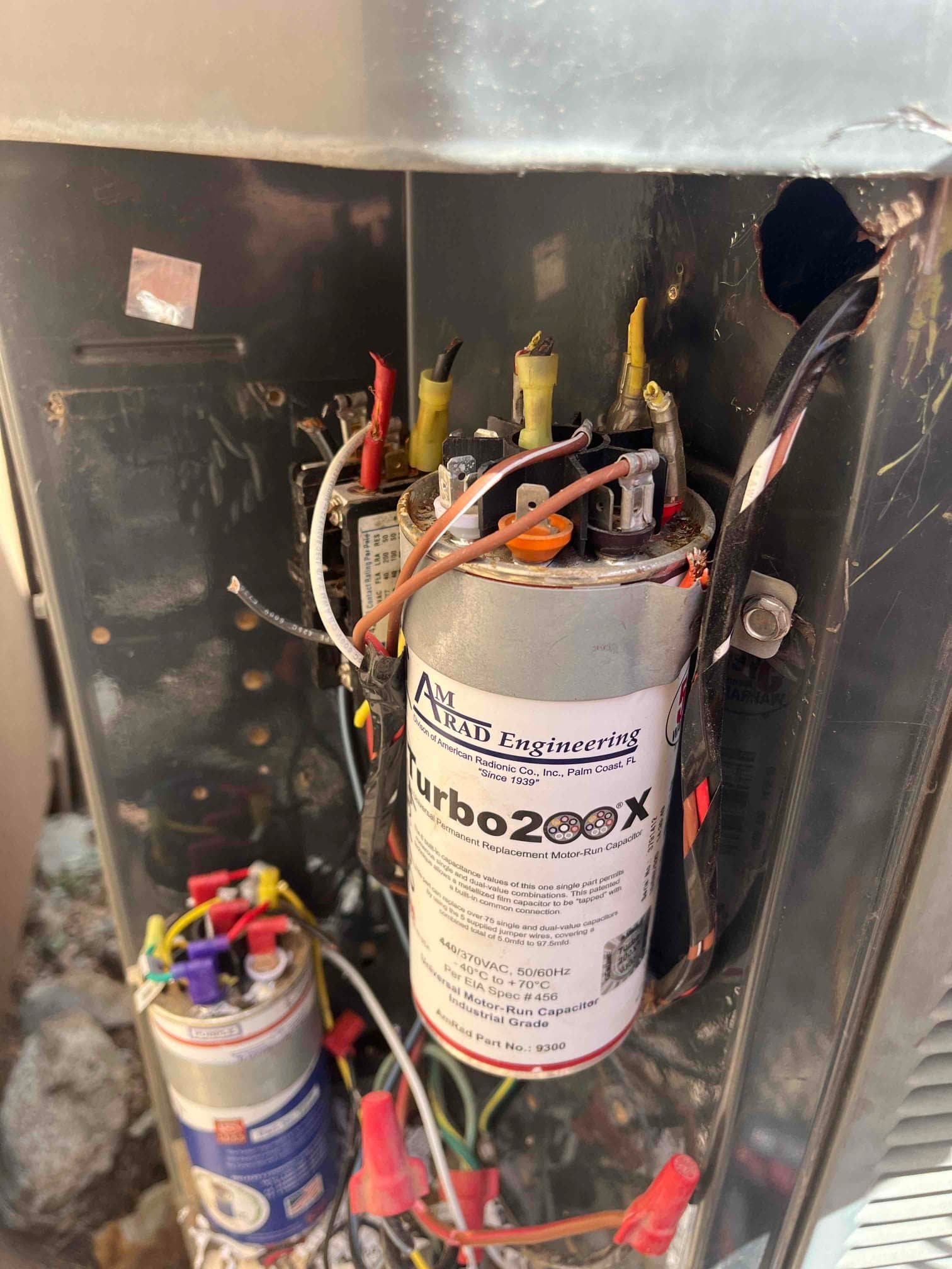 Dual motor run capacitors with connected wiring inside the outdoor condensing unit control compartment.