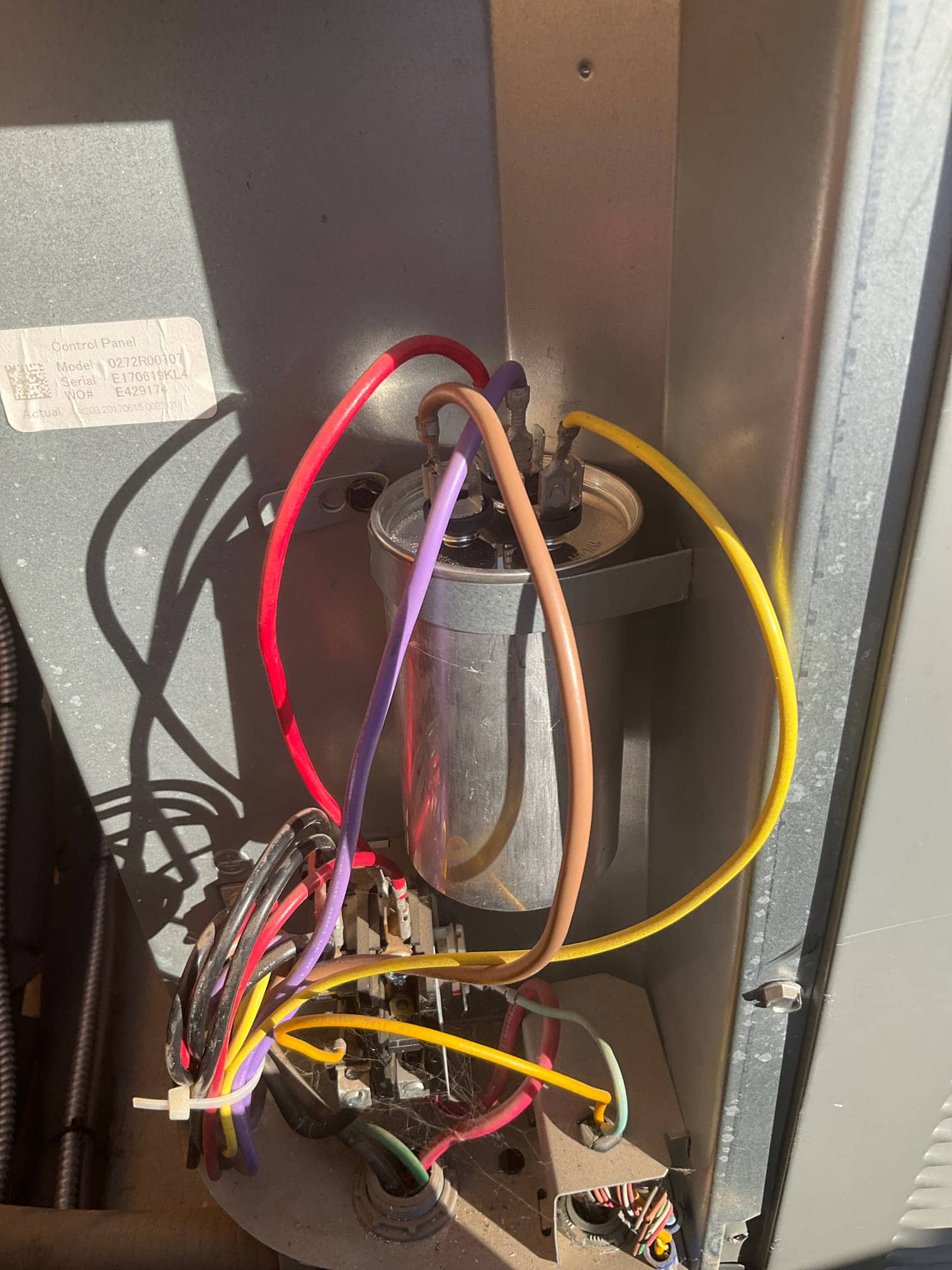 Dual-run capacitor with connected red, brown, yellow, and purple wires beside the contactor inside the condenser cabinet.