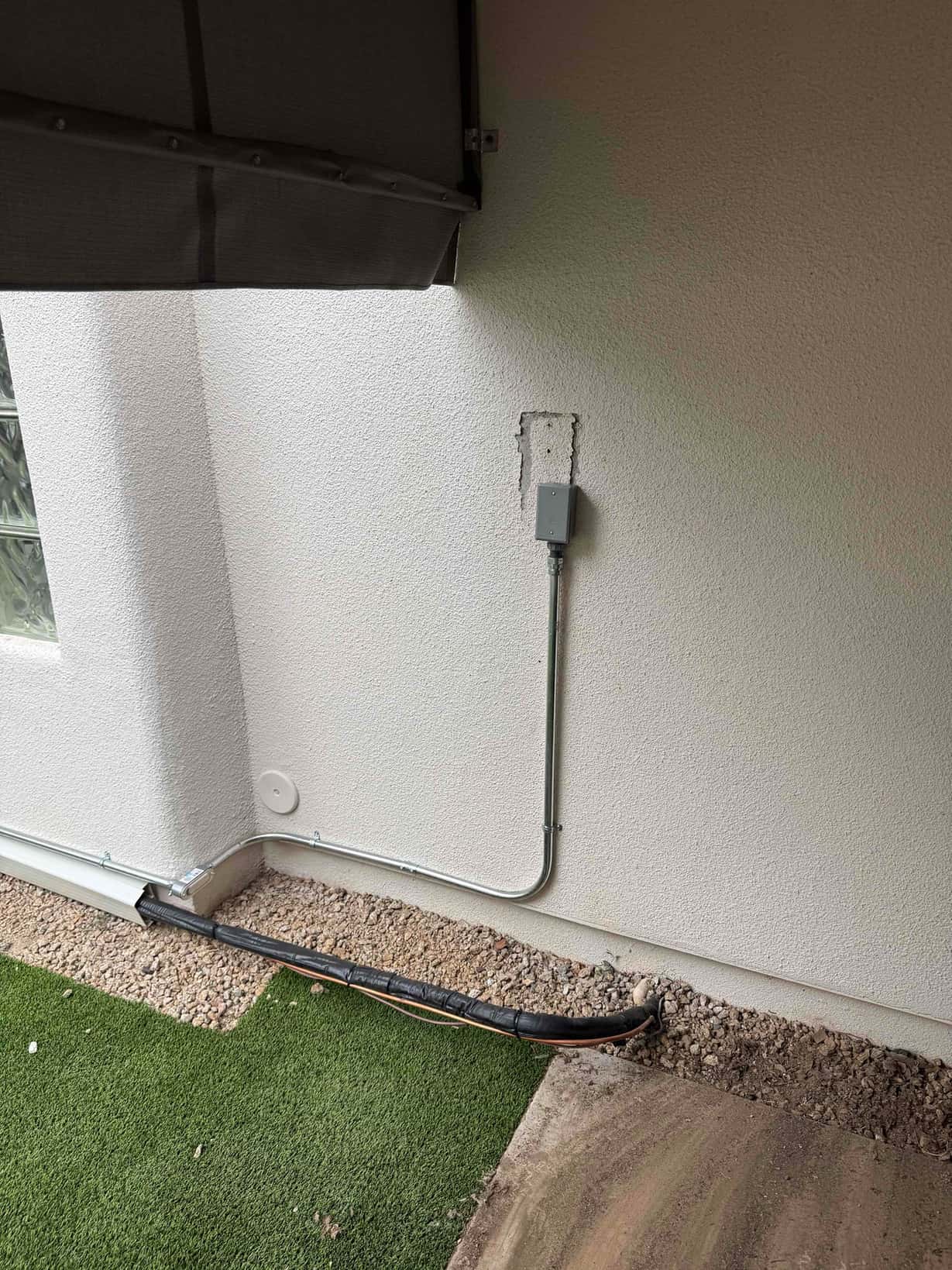 Exterior wall shows new electrical whip and conduit to a disconnect with insulated refrigerant line set routed along the foundation.