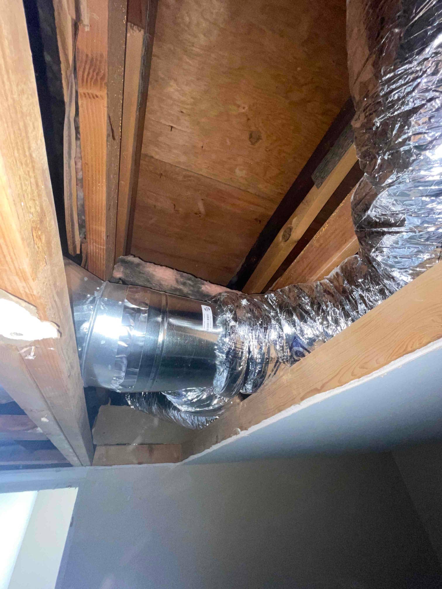 Flexible insulated duct connected to a galvanized metal elbow routed between ceiling joists during HVAC installation.