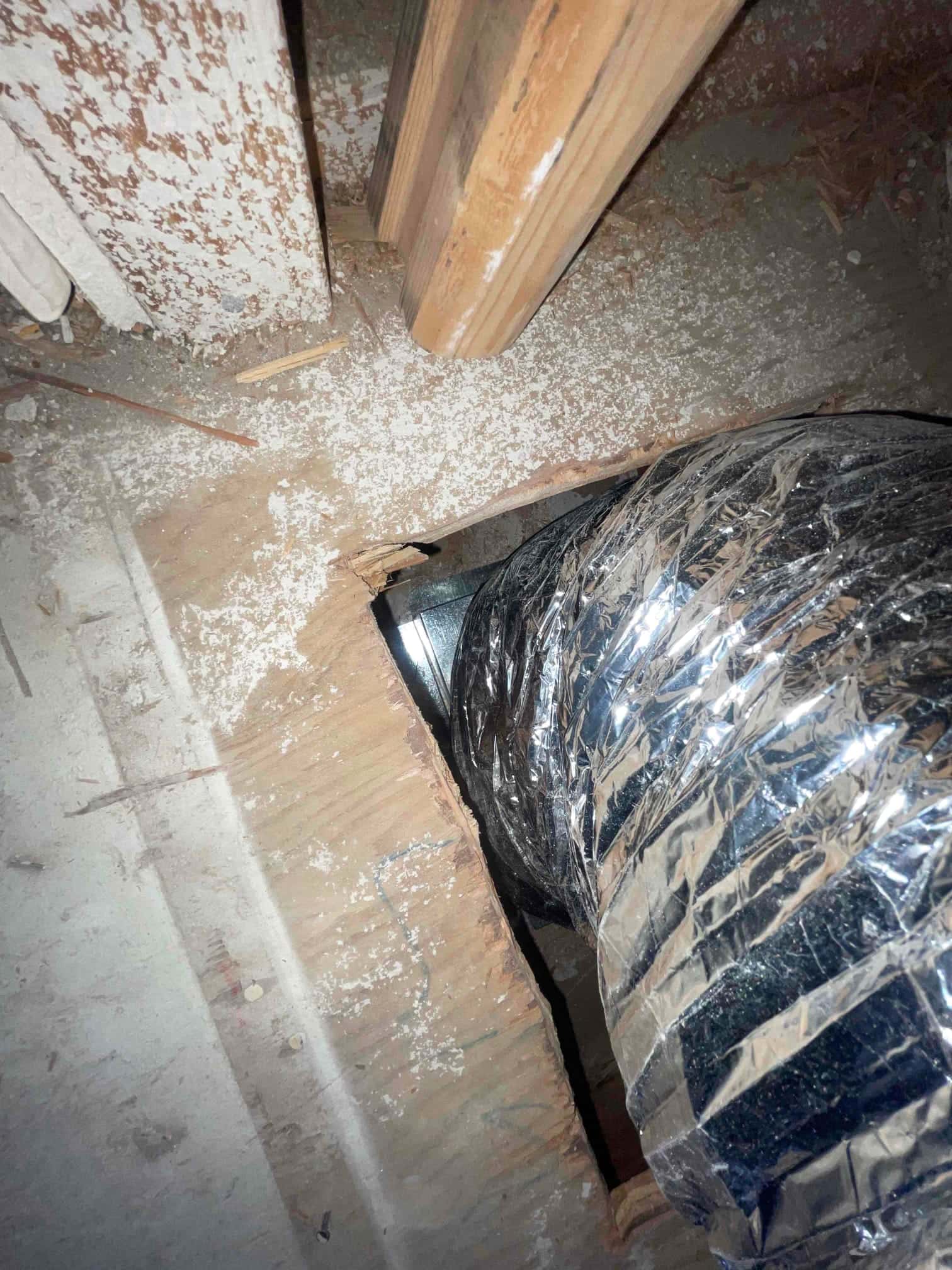 Flexible insulated duct routed through a newly cut floor opening near framing members during HVAC installation work.