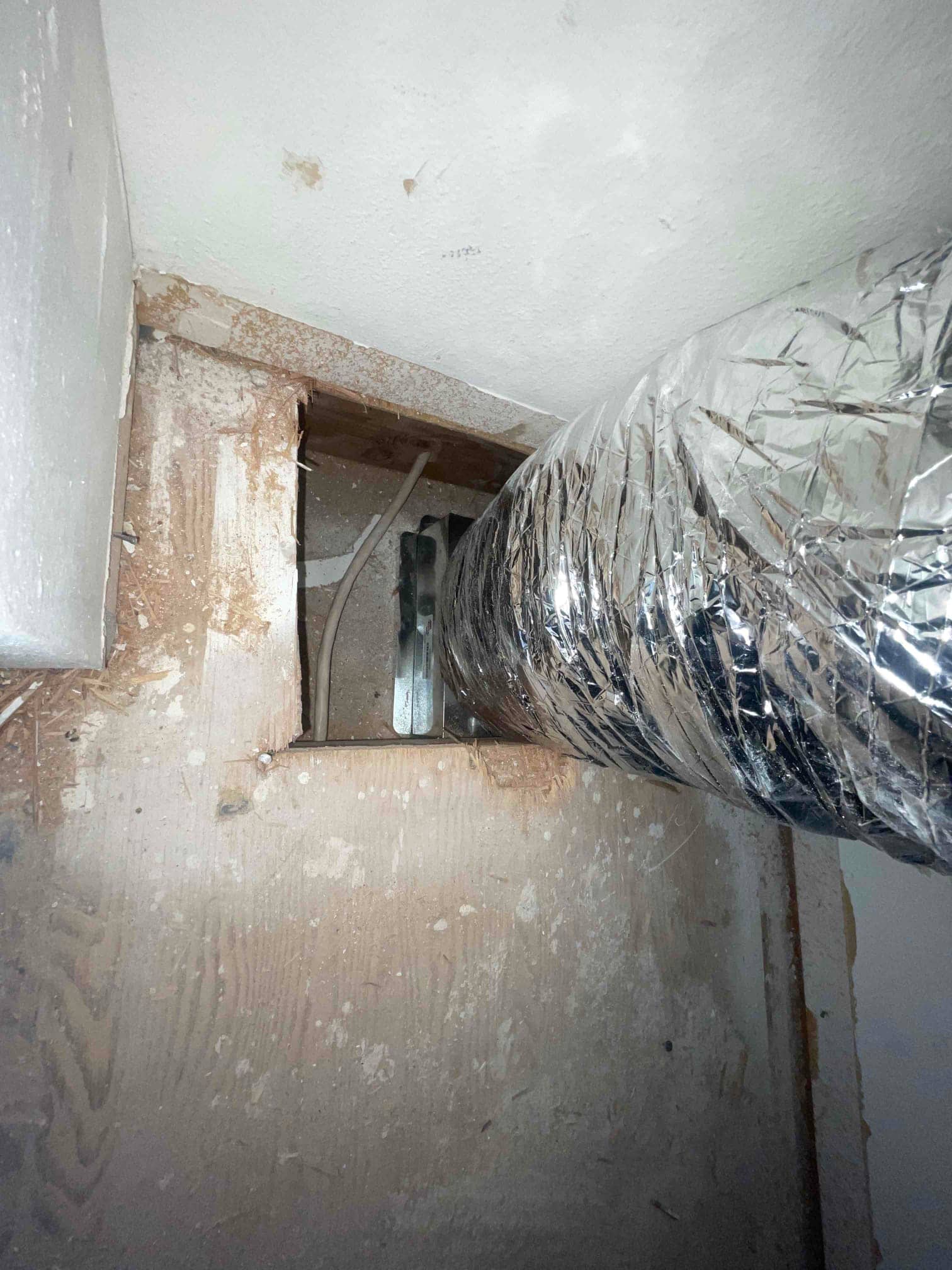Flexible insulated duct transitions through a framed opening, showing the new duct connection and surrounding framing during installation.