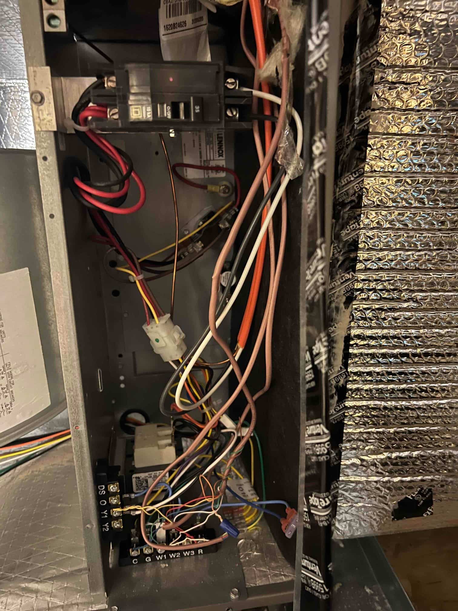 Furnace control compartment with wiring, low-voltage thermostat terminals, breaker, and duct insulation at right.