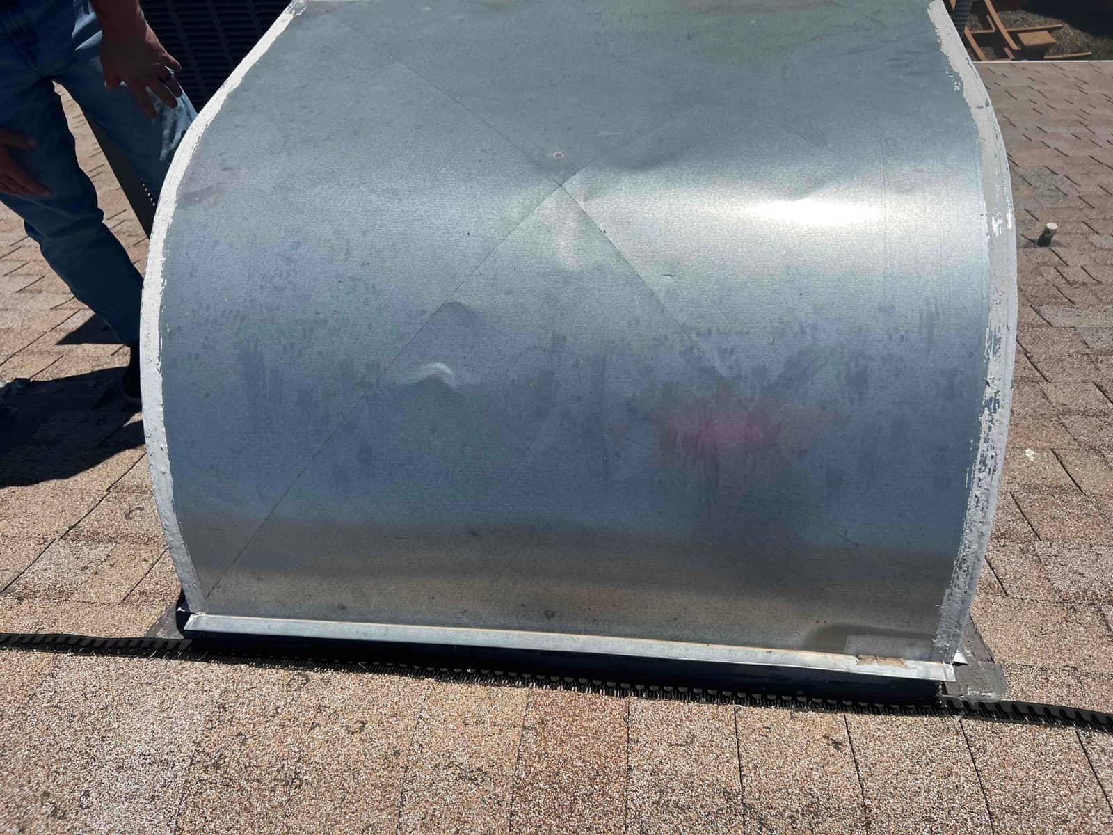 Galvanized rooftop duct enclosure seated on shingles, with sealant along the perimeter flashing.