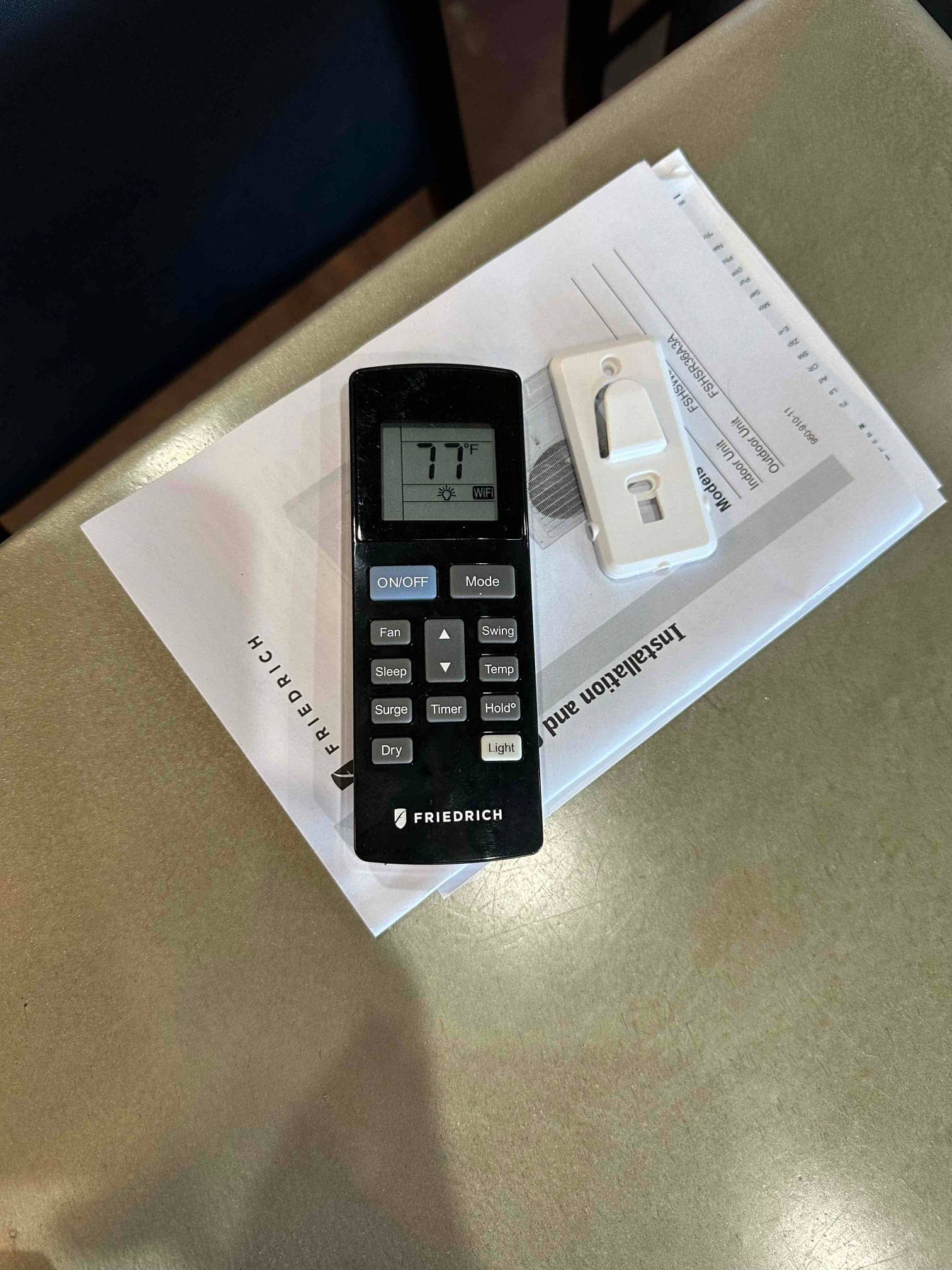 Handheld mini-split remote on installation paperwork showing 77°F on the display during system setup.