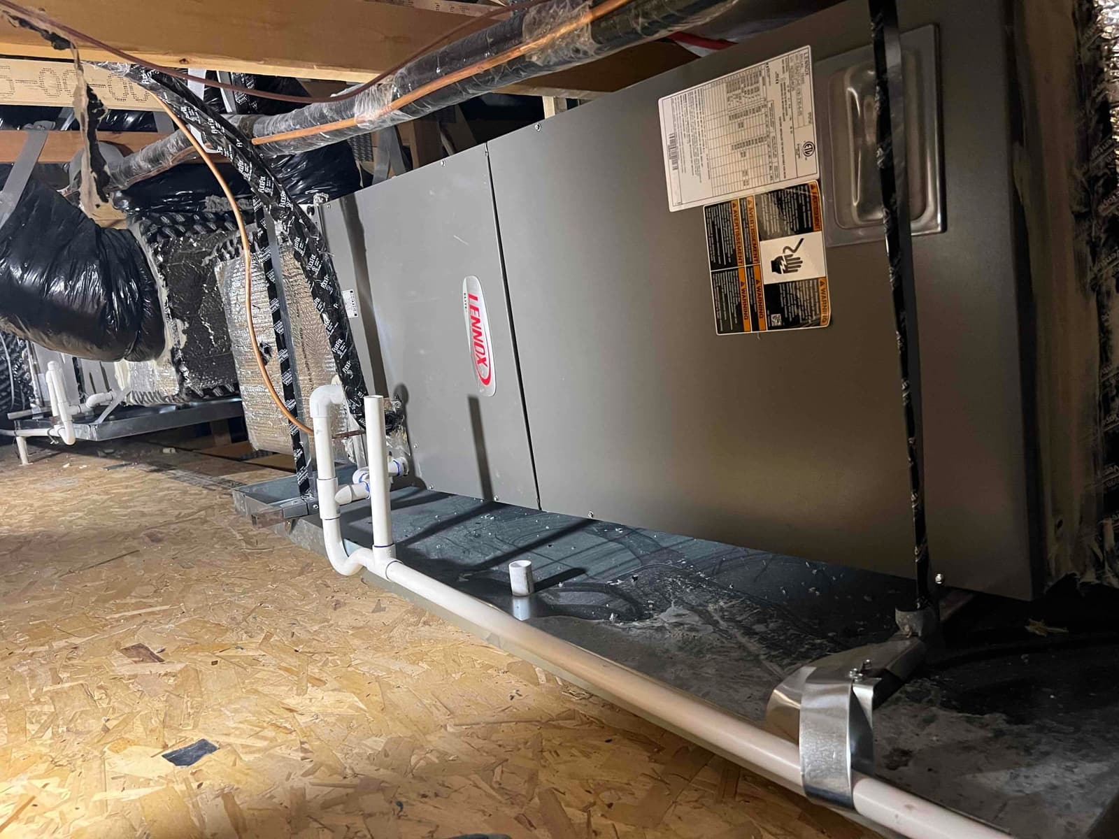 Horizontal air handler in attic with insulated duct connections, copper refrigerant line, and PVC condensate drains over a secondary drain pan.